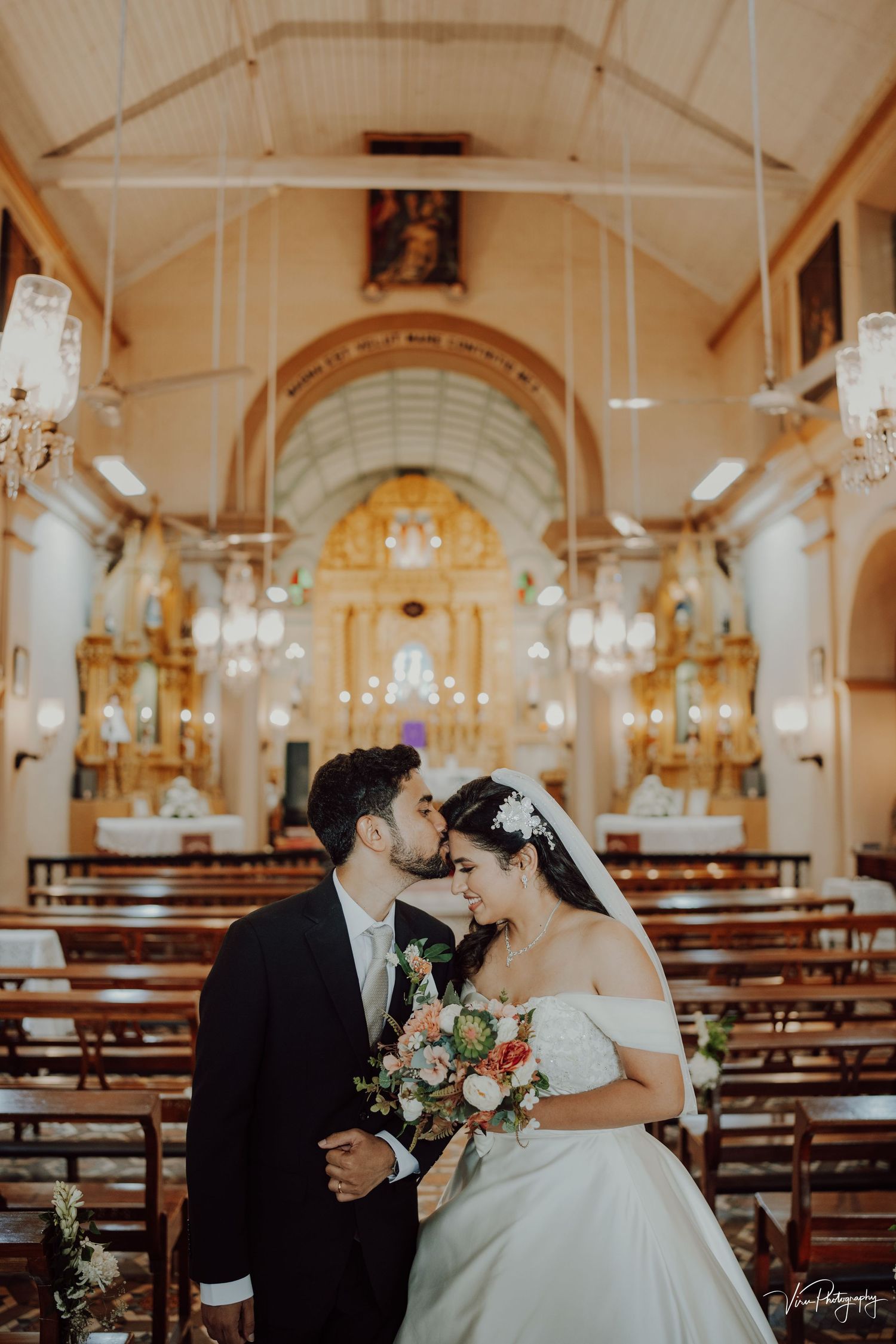 A romantic wedding ceremony captured inside an ornate Catholic church with golden altar and glowing chandeliers.
