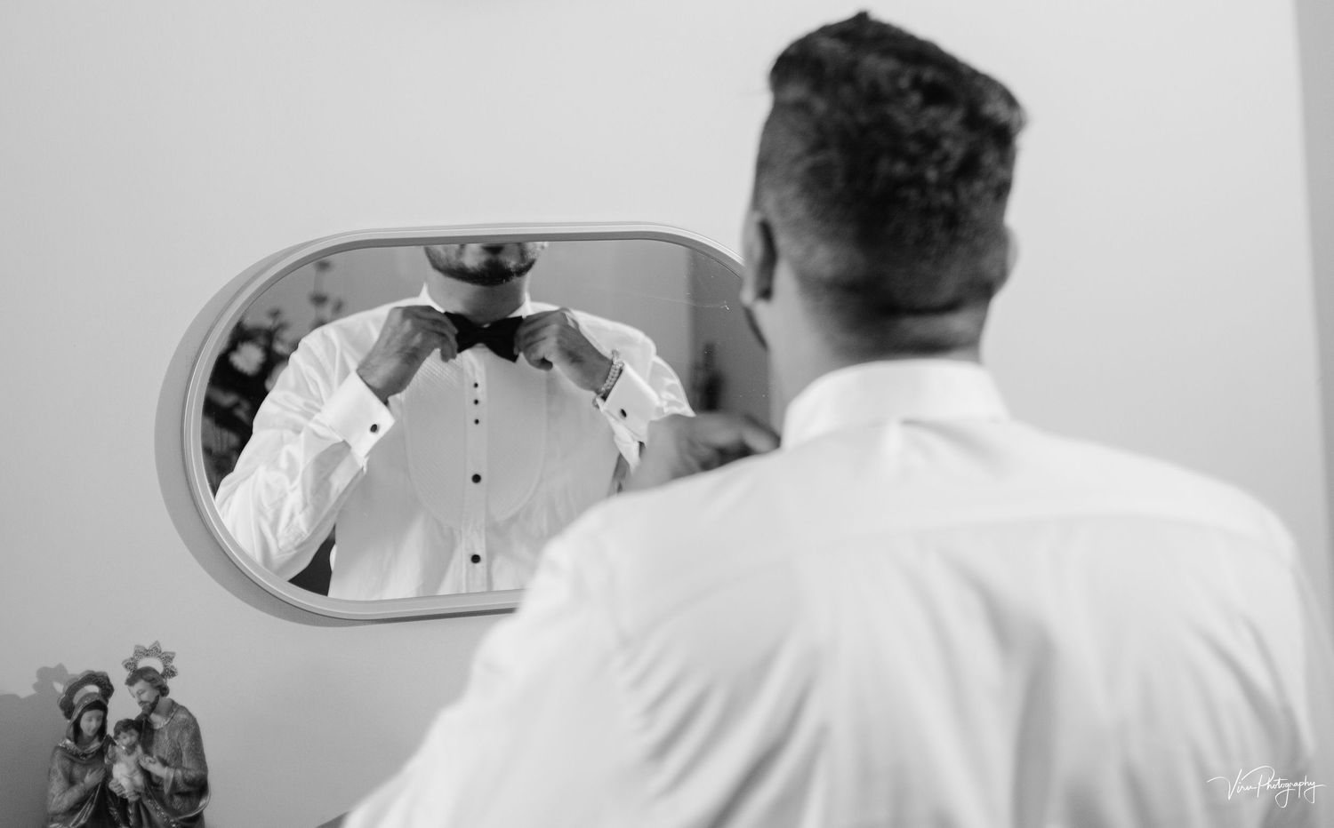 Back view of a person wearing a white shirt looking at themselves in an oval mirror mounted on a grayscale wall.