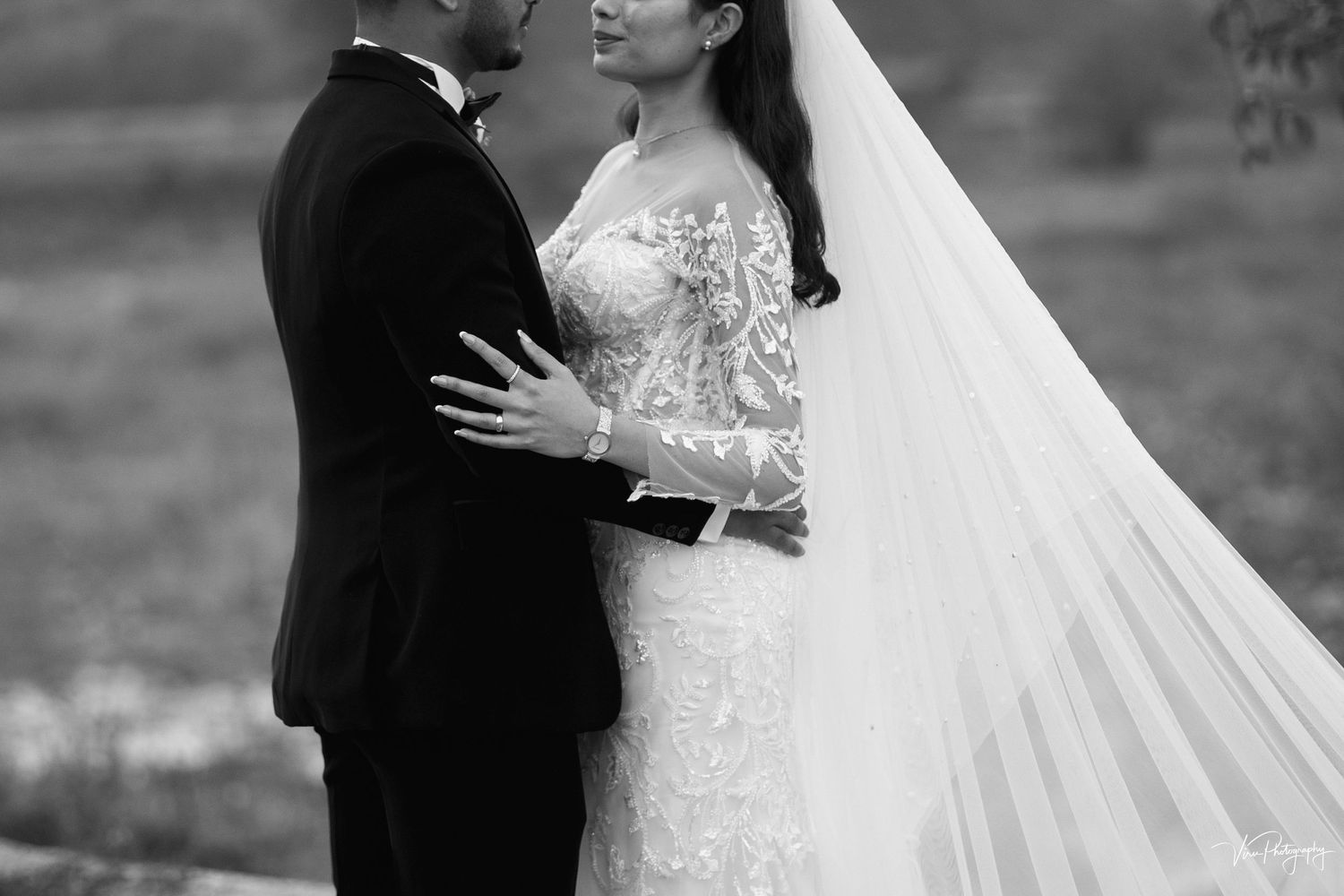 A romantic black and white wedding photo shows a couple embracing outdoors with a flowing veil and lace wedding dress.
