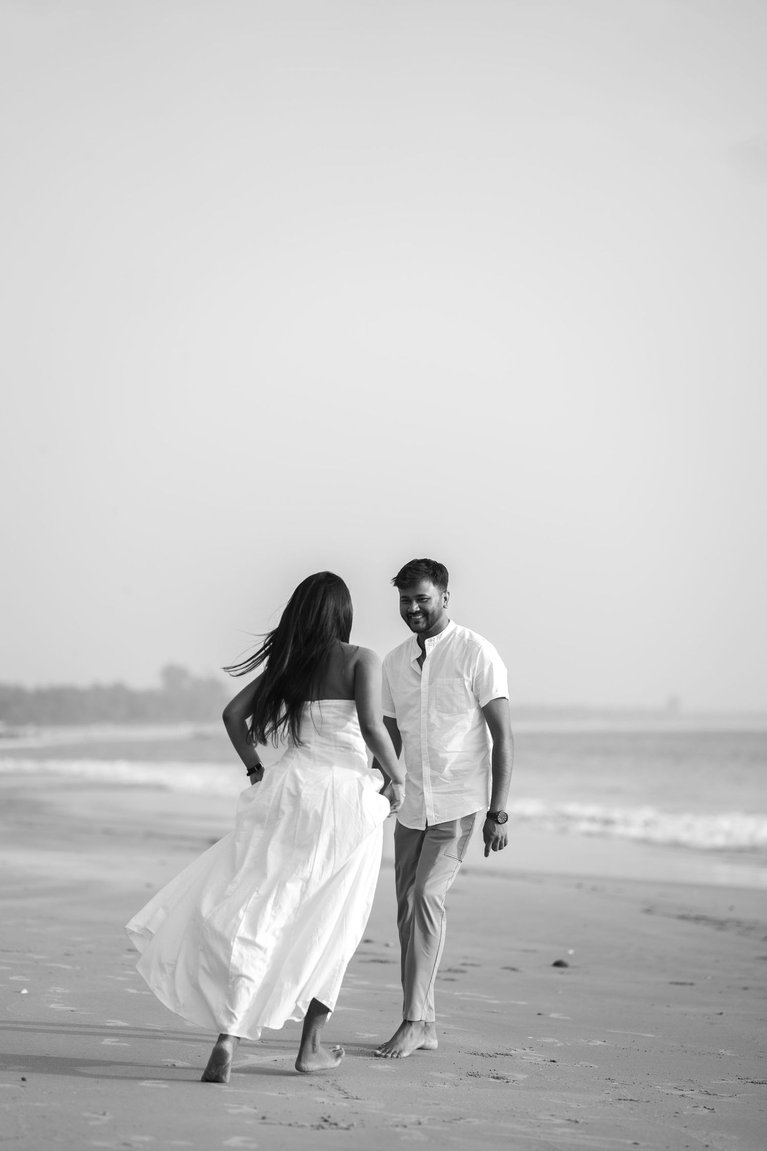 A romantic black and white photo sequence of a couple in white outfits playing and walking along a misty beach.