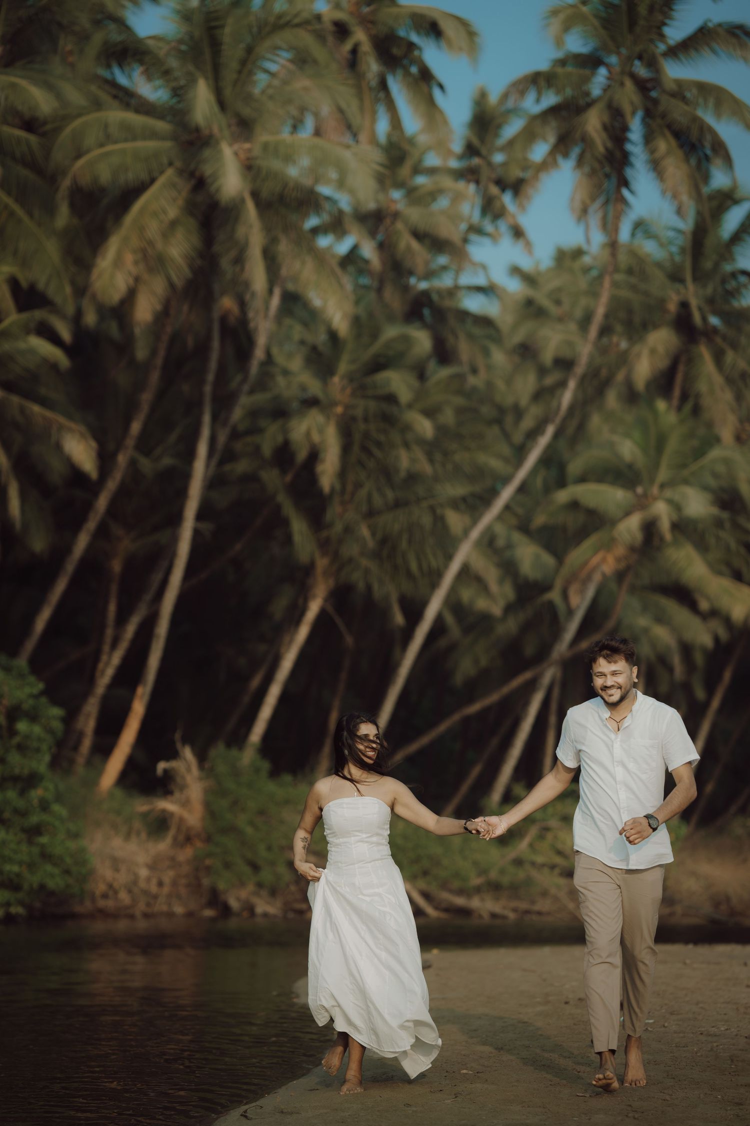 A couple strolls hand in hand along a tropical beach lined with swaying palm trees at sunset.