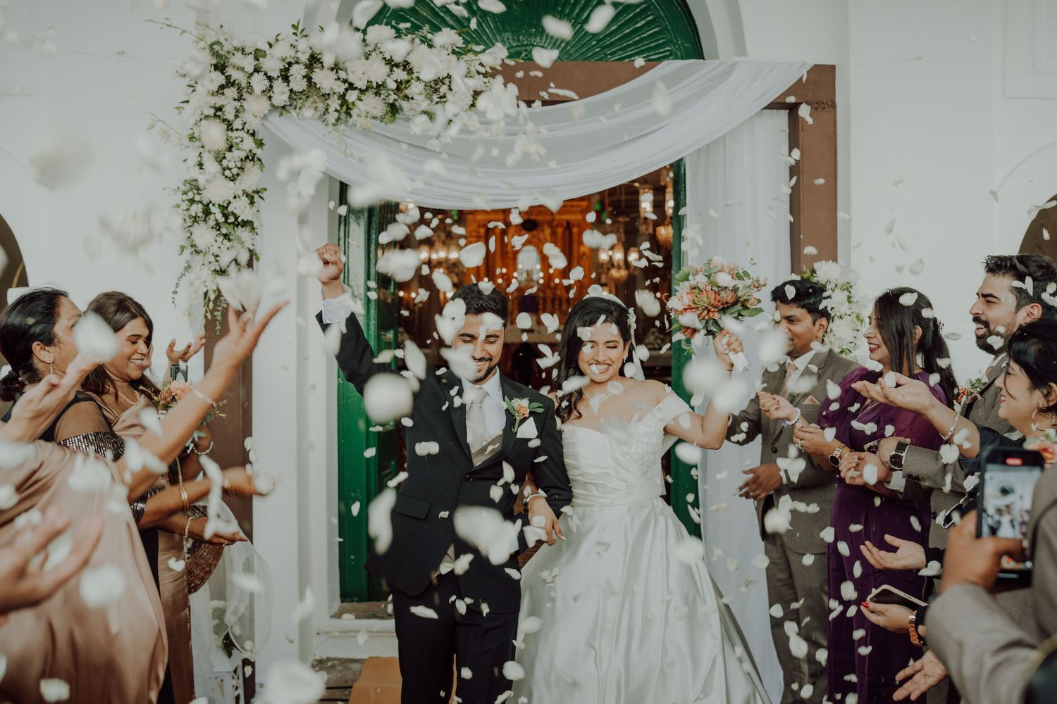 Wedding celebration moment with confetti shower and floral arch decorations.