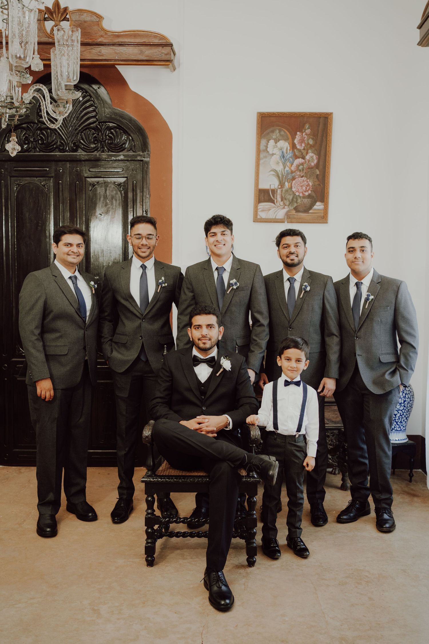A wedding party in suits posing for a formal group photo with vintage decor.