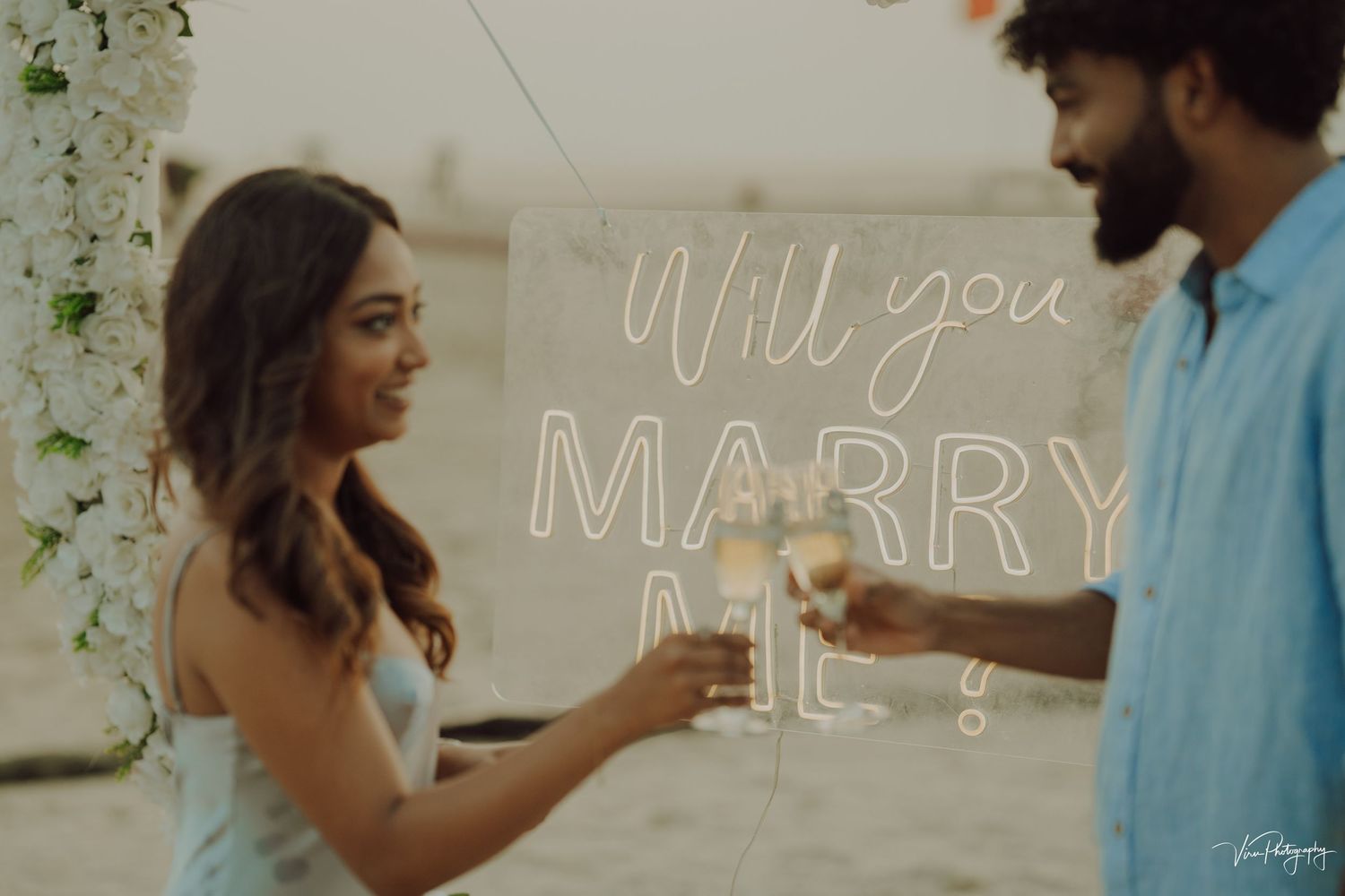 Marriage proposal scene with champagne glasses in front of illuminated 