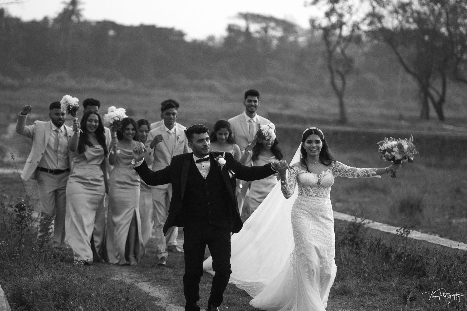 A wedding party walks together across a grassy field in black and white photography.