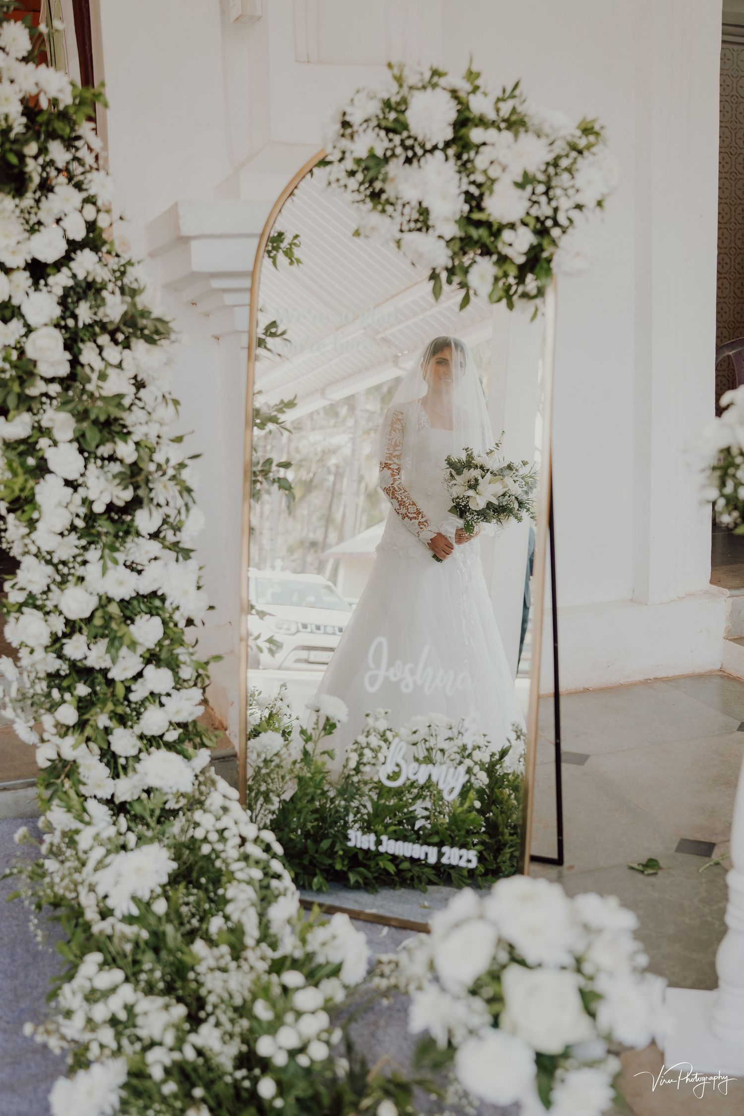 Elegant wedding decor with white floral arrangements and greenery framing a decorative mirror display on a porch.