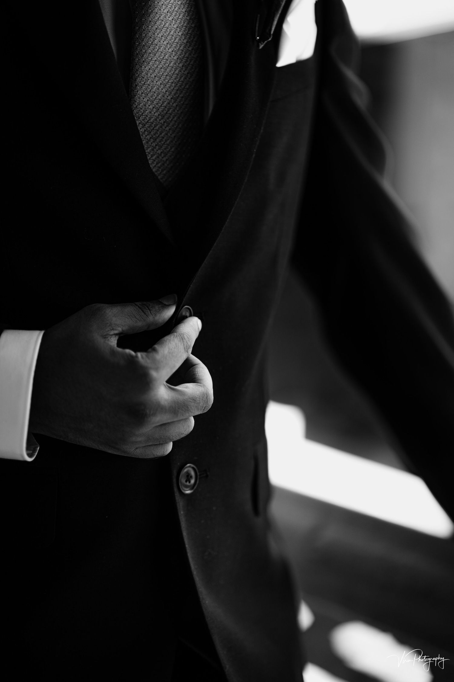 Black and white detail shot of a hand adjusting a button on a formal dark suit jacket.