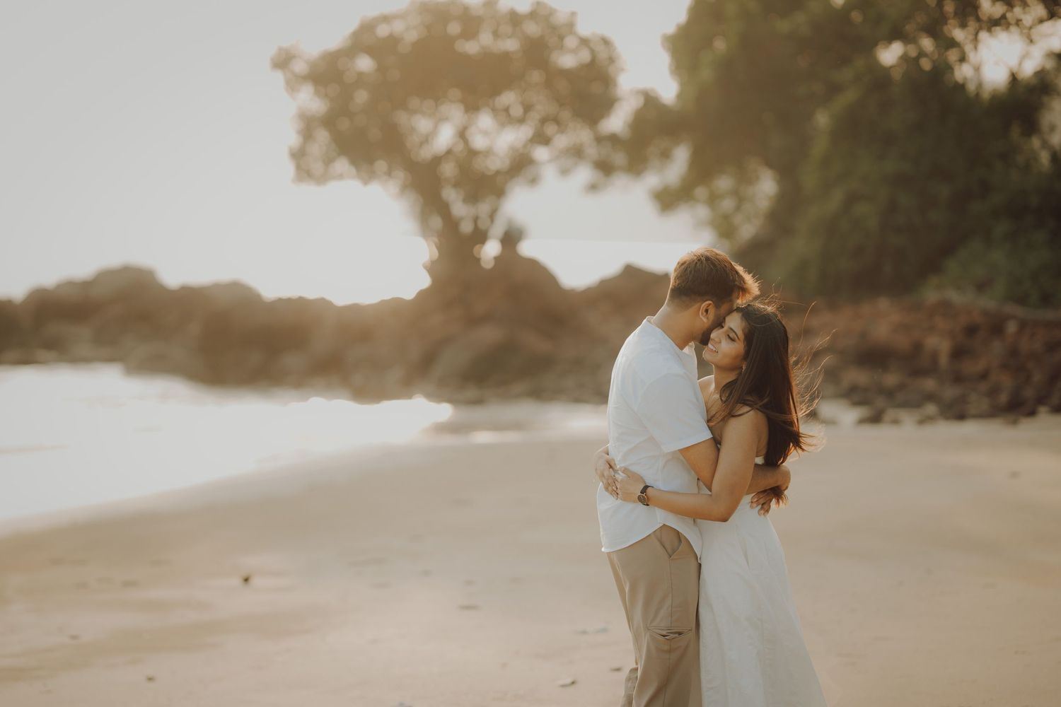 A couple shares a romantic moment on a misty beach at sunset during their wedding photo session.