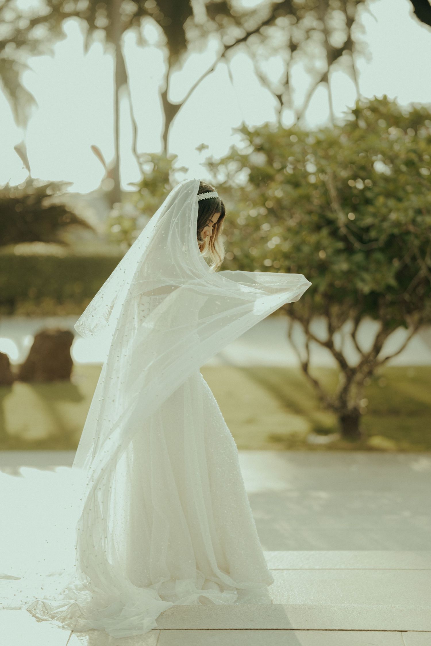 Ethereal bride in flowing white gown and veil twirls gracefully in a garden setting creating a dreamy motion effect.