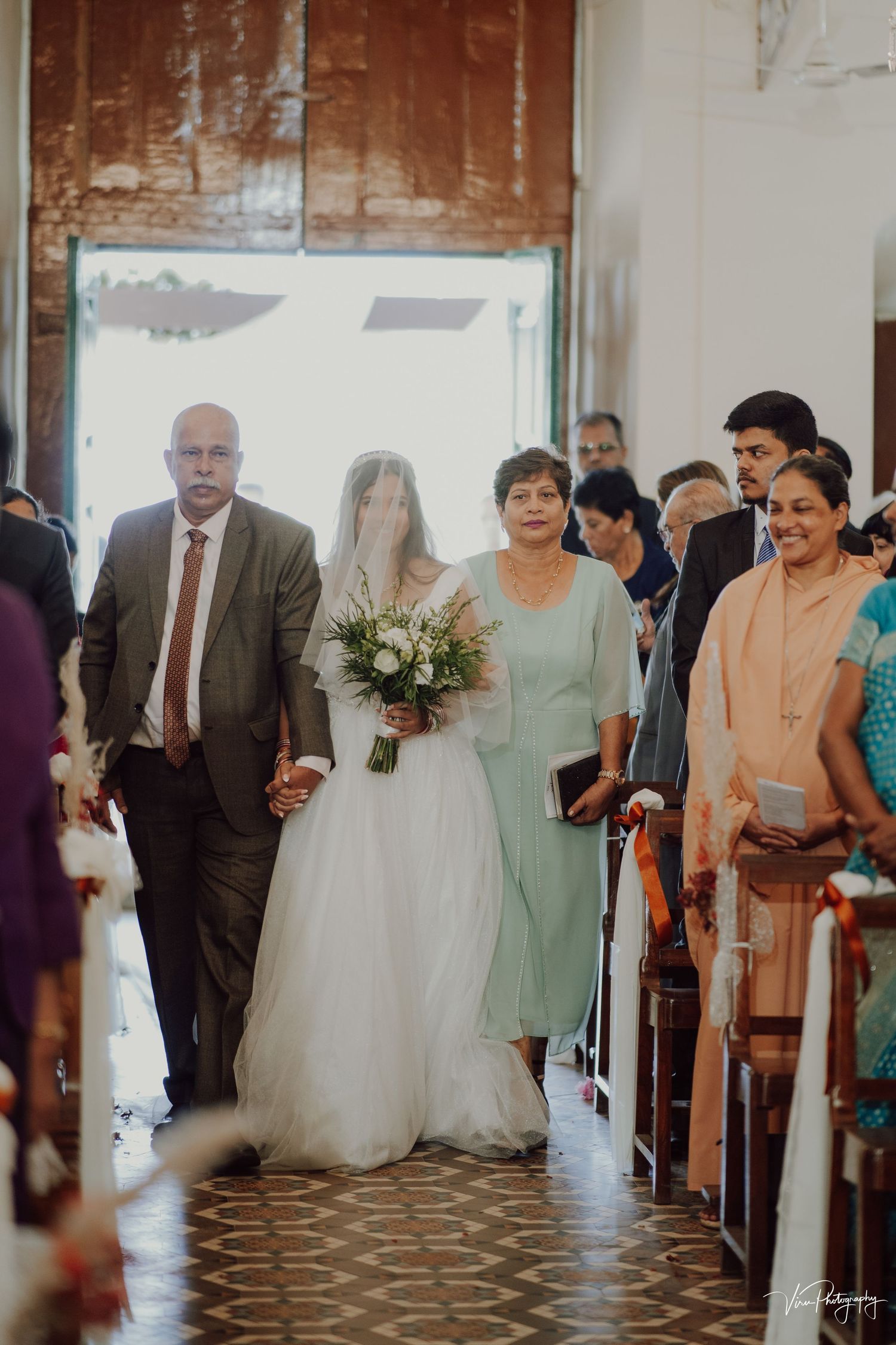 A traditional wedding processional in a church with guests watching as a bride enters with her escort down the aisle.