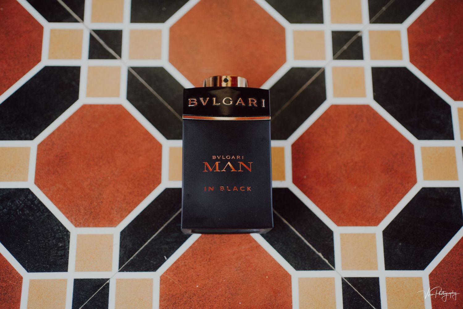 A Bvlgari Man in Black cologne bottle sits on a geometric black, orange and beige tiled surface.