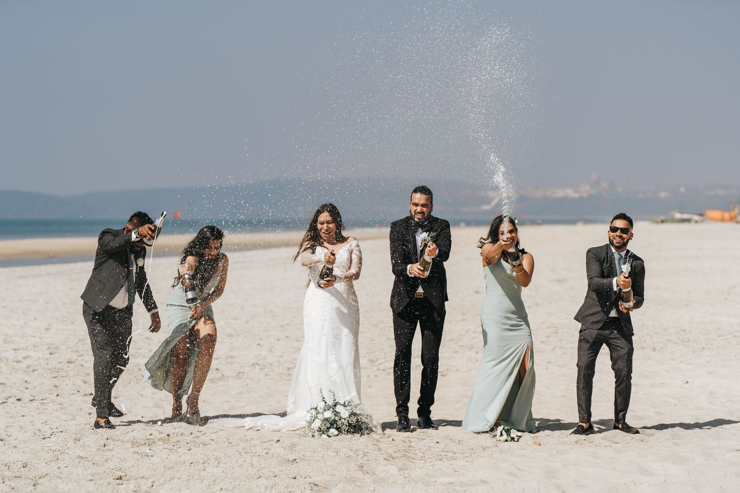 A wedding party poses playfully on a scenic white beach.