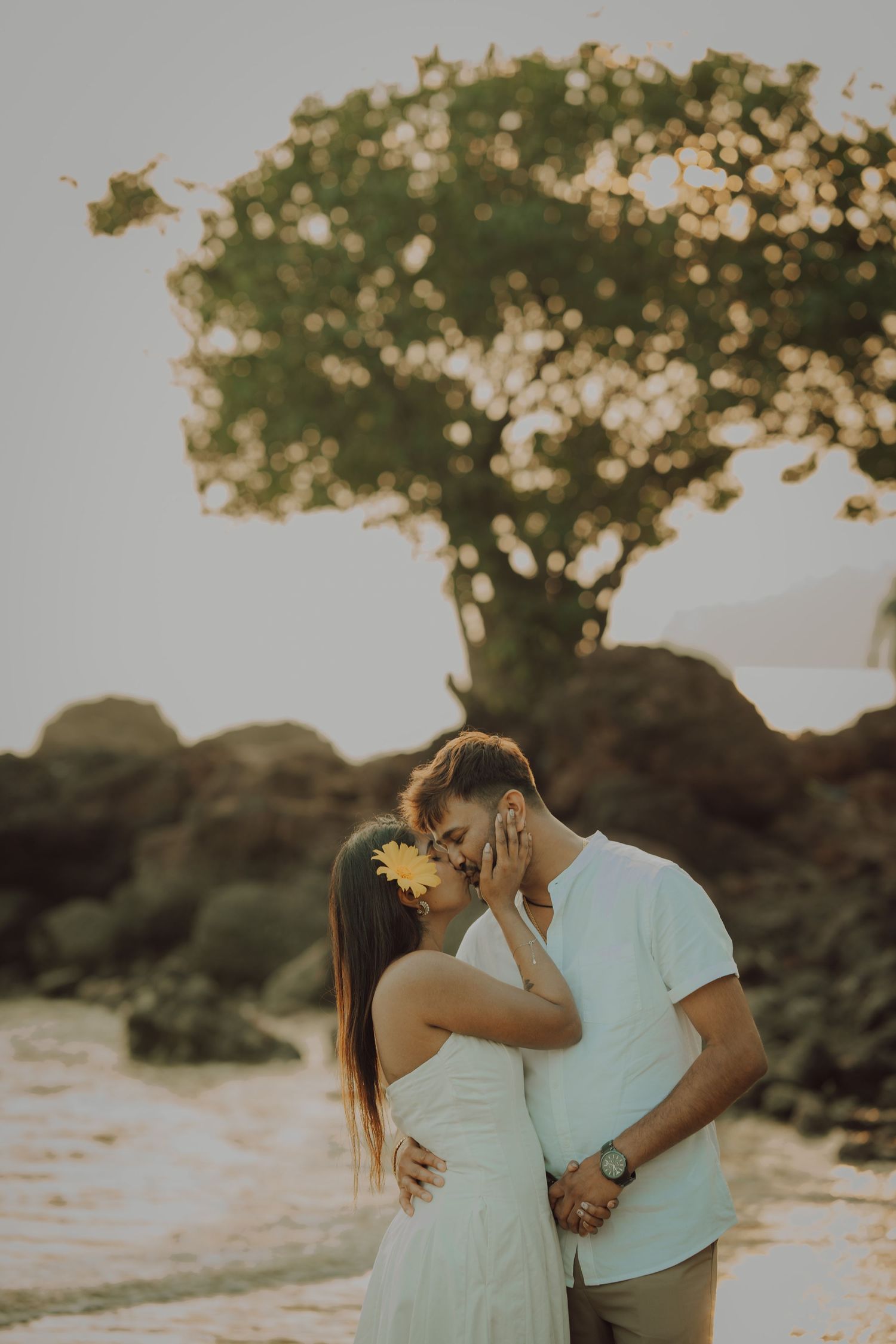 A romantic couple embraces at sunset with trees silhouetted in the background during a golden hour photoshoot.