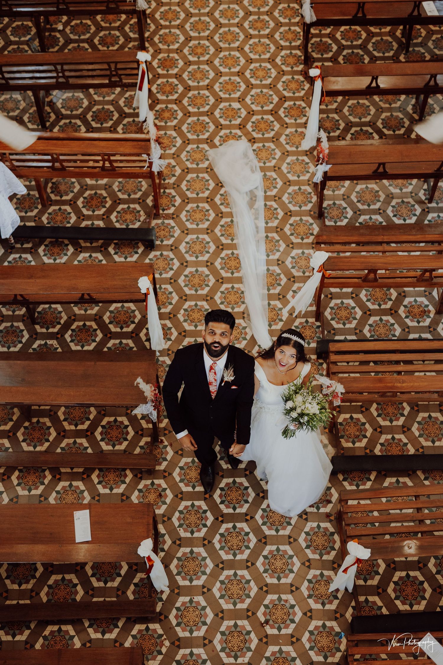 Overhead view of a wedding couple lying on vintage hexagonal patterned carpet in church pews.