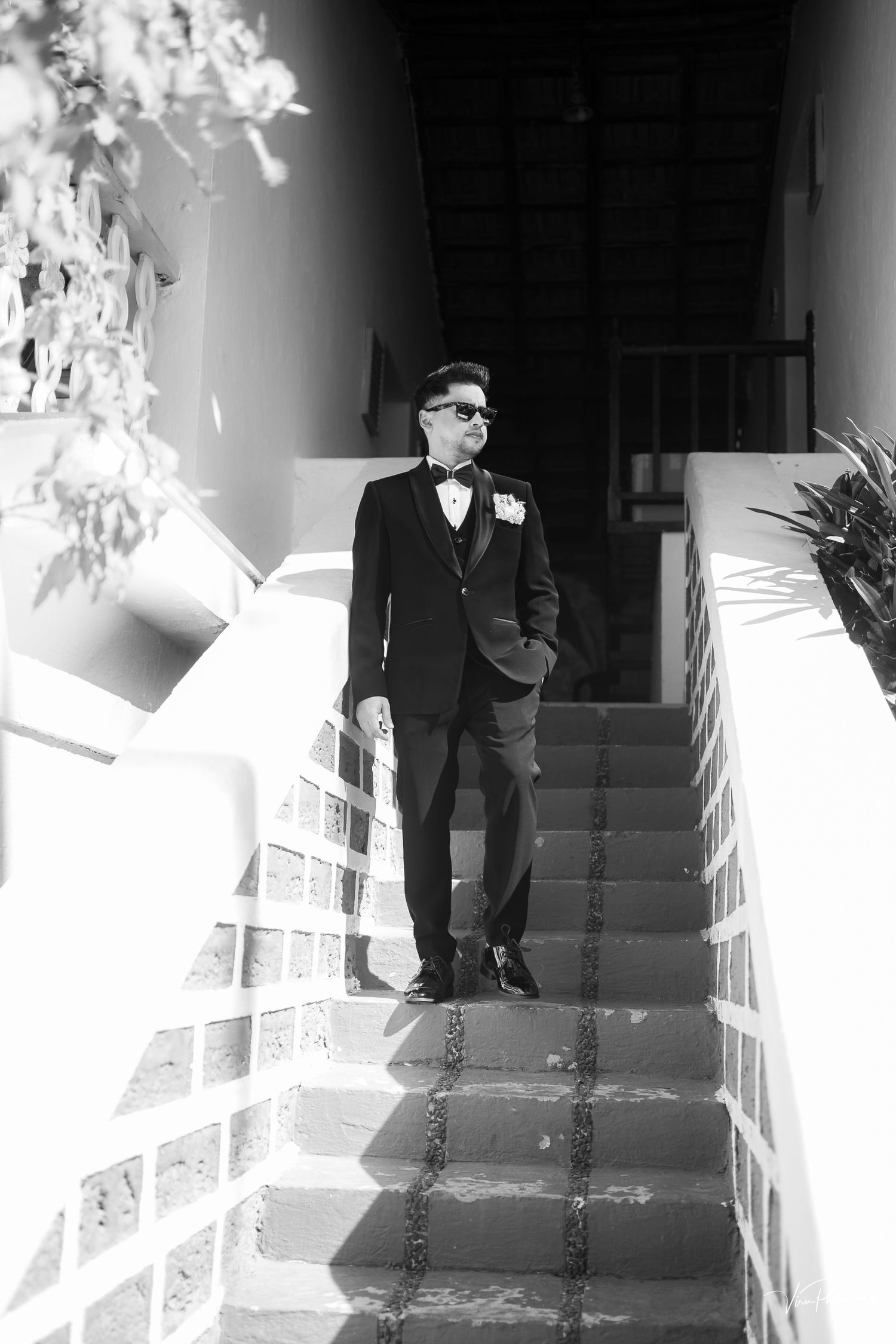 Black and white photo of someone in a formal tuxedo with bow tie standing on white steps in dramatic lighting.