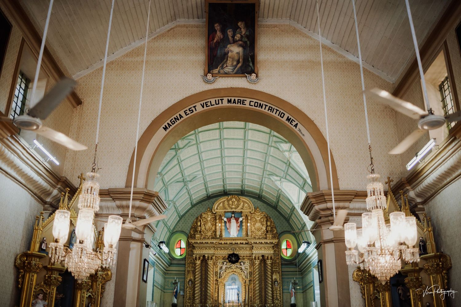 Ornate church interior with elegant chandeliers and arched ceiling leading to a gilded altar beneath soft lighting.