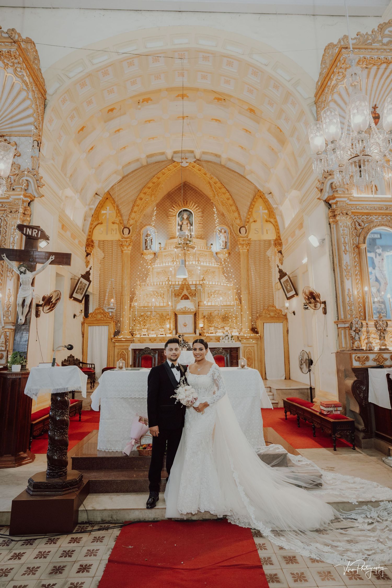 Interior of ornate Catholic church with baroque altar, crystal chandelier, and red carpet leading to gilded sanctuary.