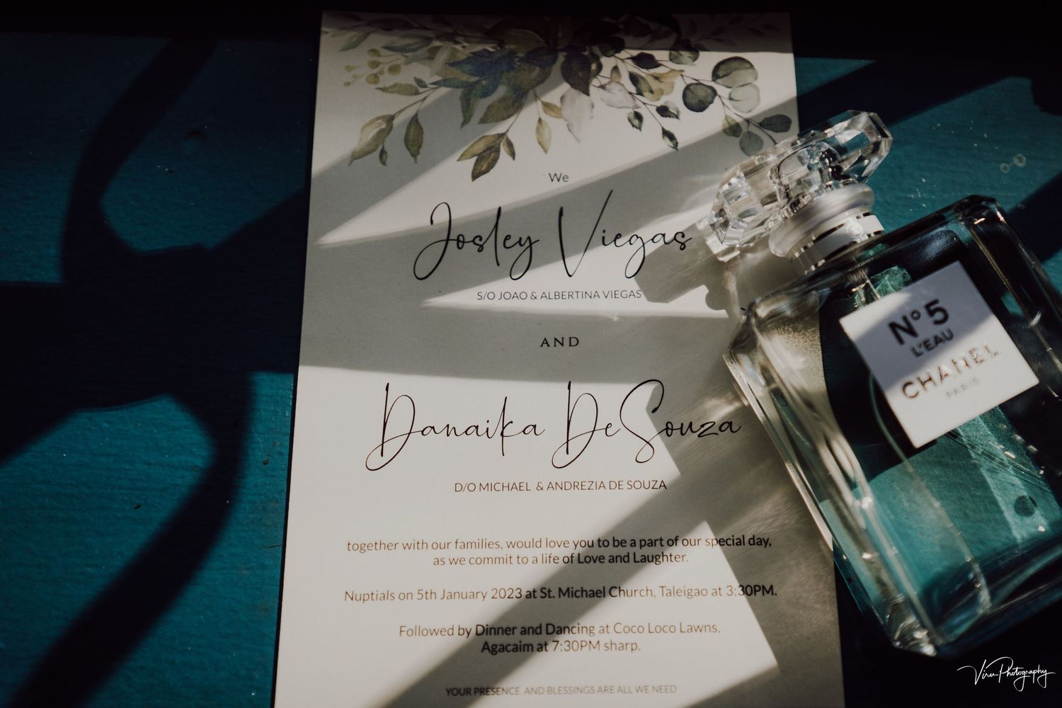 A wedding invitation with calligraphy text lies next to a blue perfume bottle in elegant lighting.