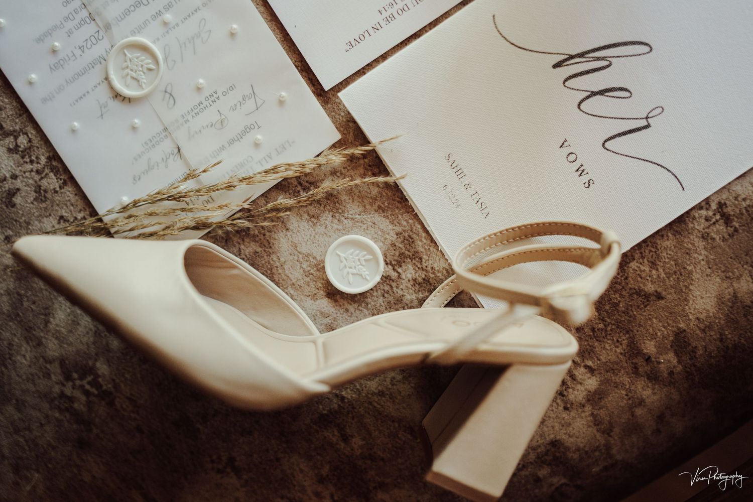 Elegant white bridal shoes with block heels displayed alongside wedding stationery and rings on a textured surface.