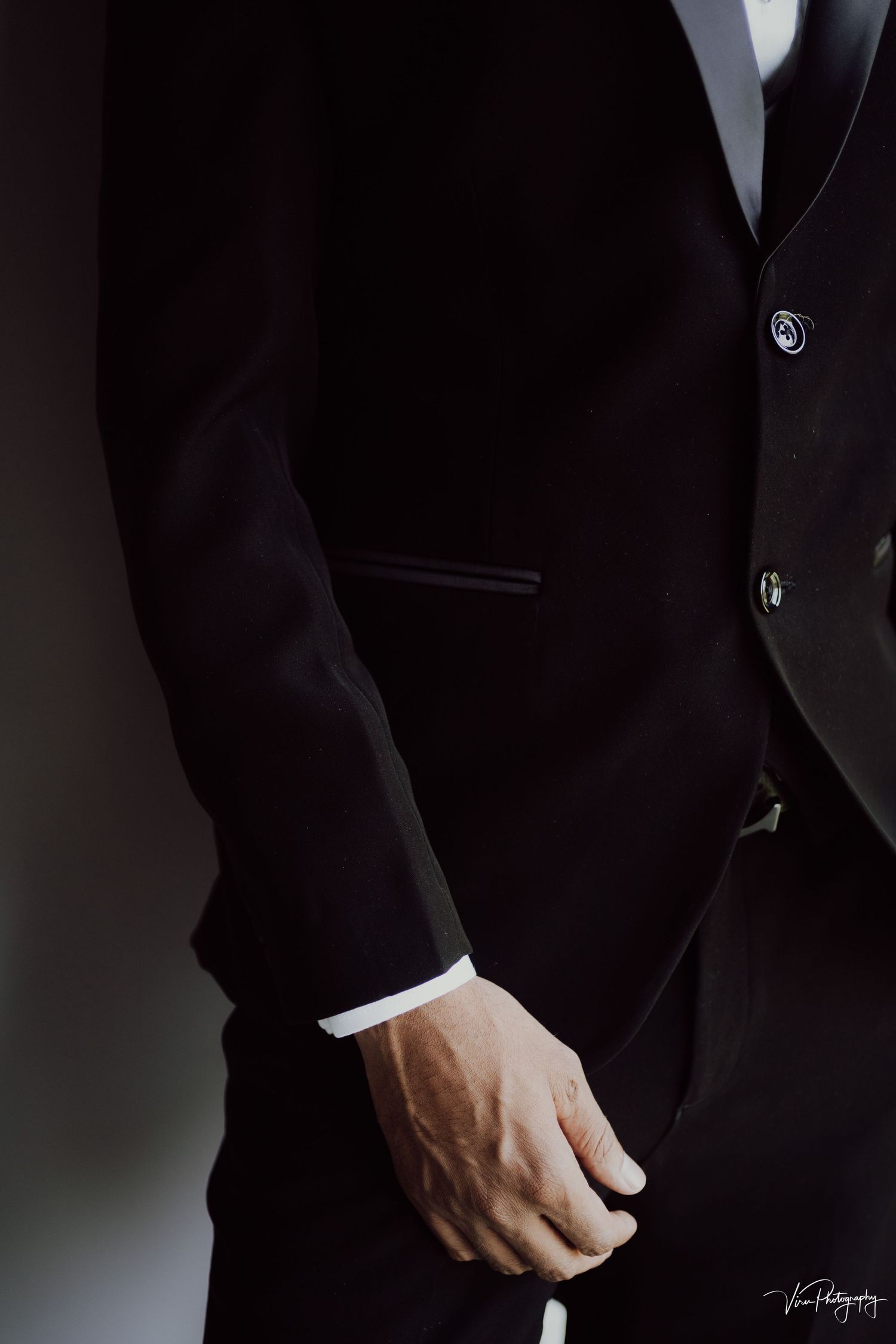 Close-up detail shot of a black formal suit jacket with white dress shirt cuff showing at the wrist.