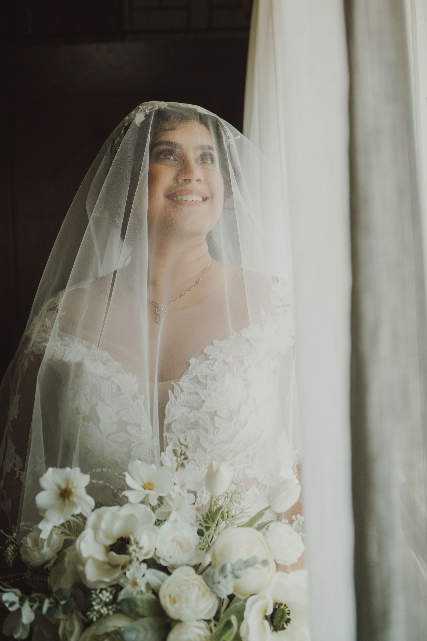 Beautiful bridal portrait with delicate lace veil and white floral bouquet in soft natural lighting.