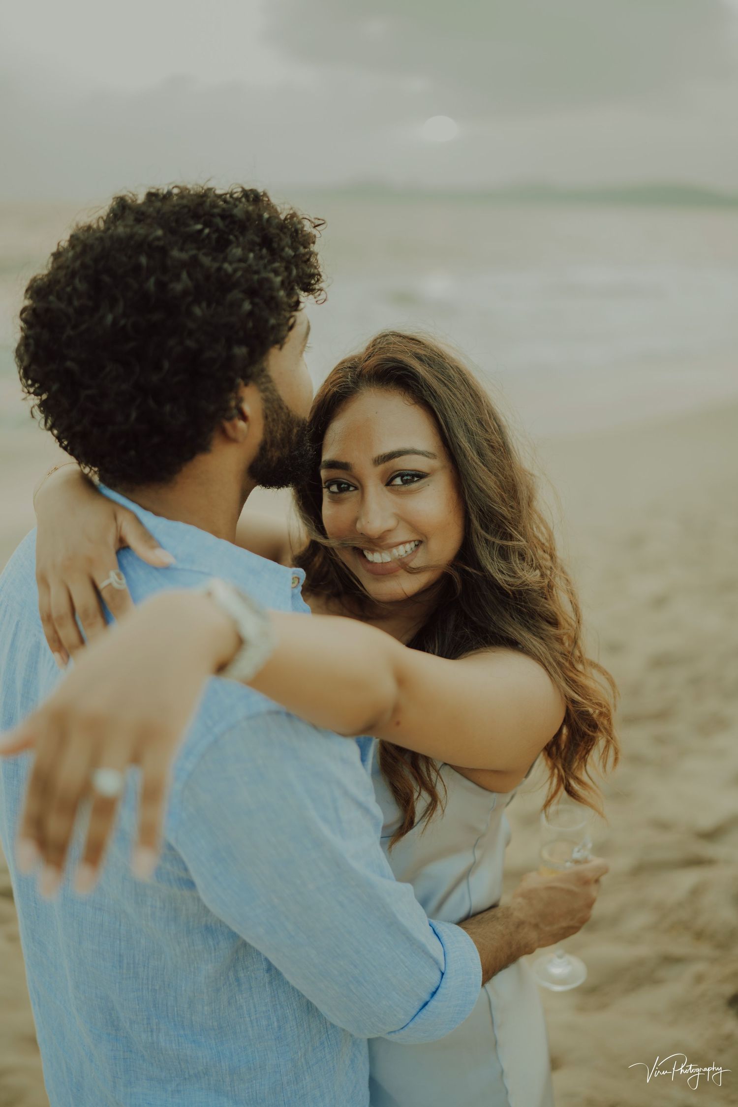 A romantic couple embraces on a misty beach during golden hour.