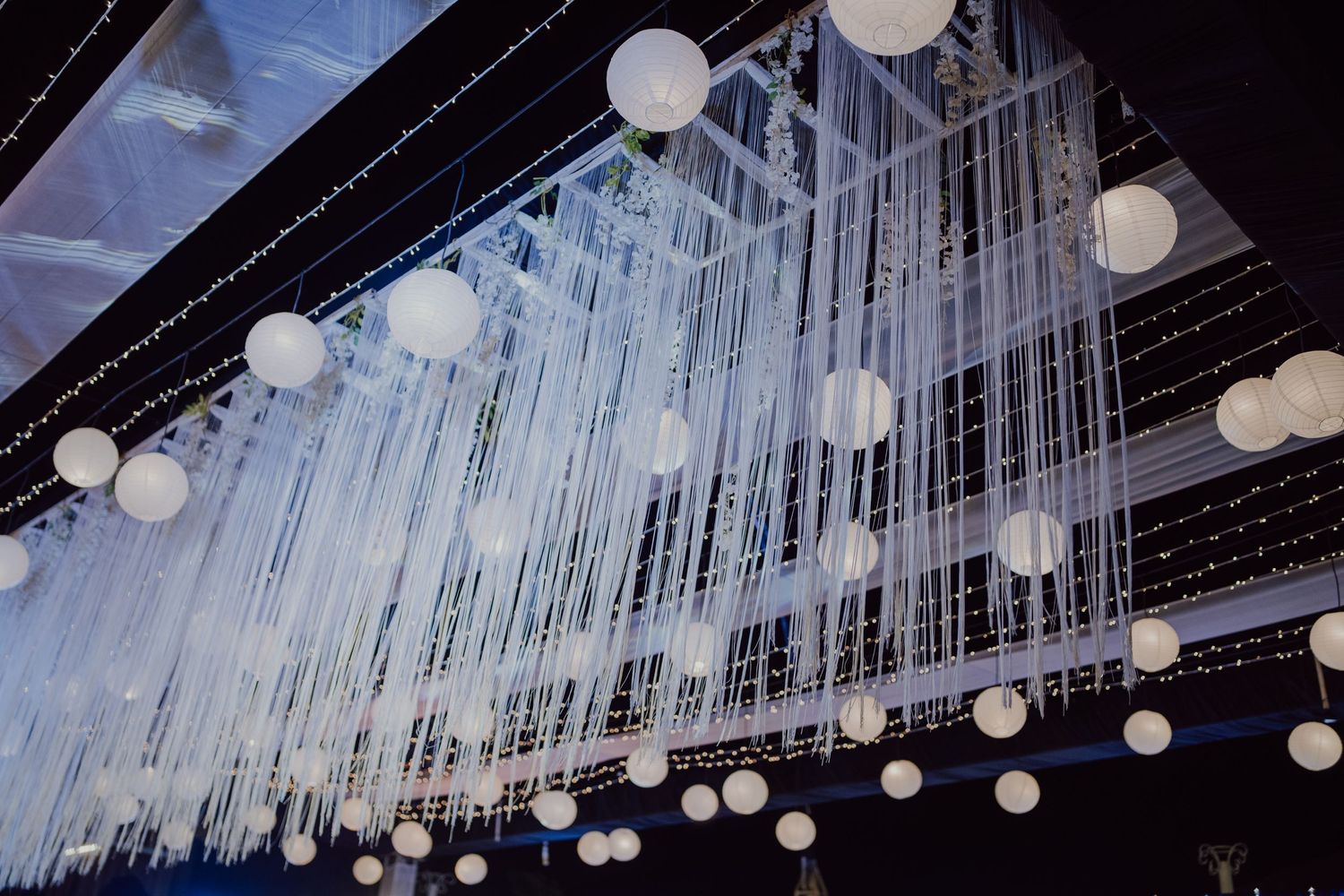 Modern wedding reception decor featuring hanging white lanterns and string lights.