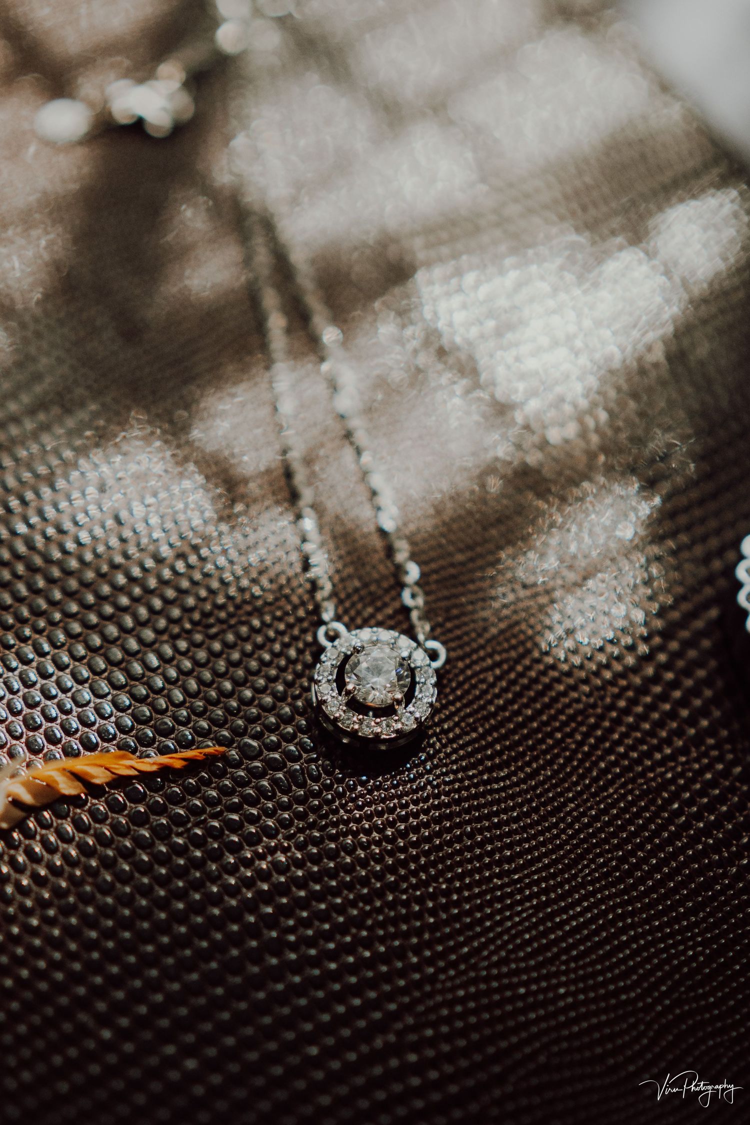 A delicate diamond pendant necklace rests on a textured brown surface with soft bokeh lighting effects.