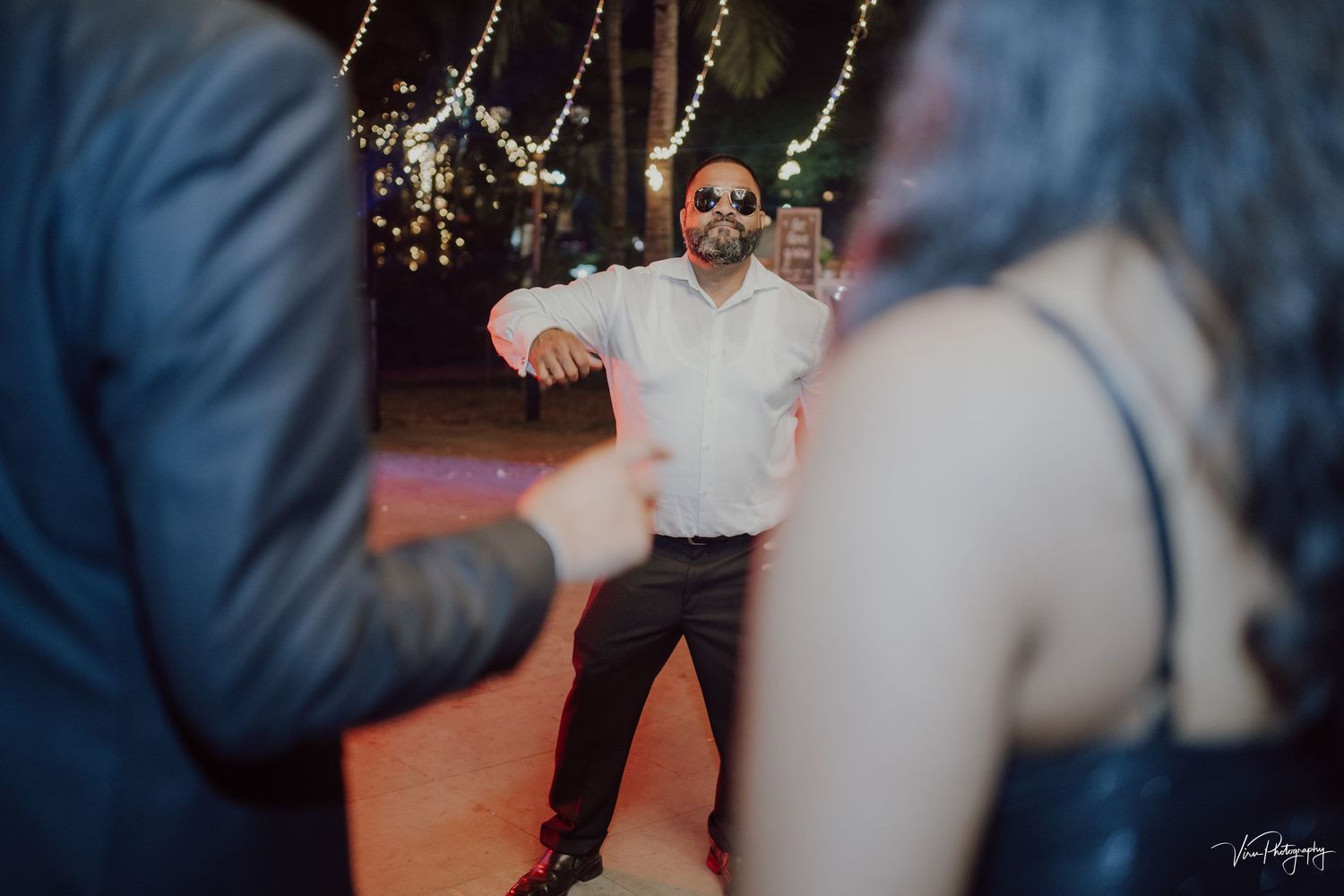 Guest dances enthusiastically on a red floor under hanging string lights at an evening celebration event.