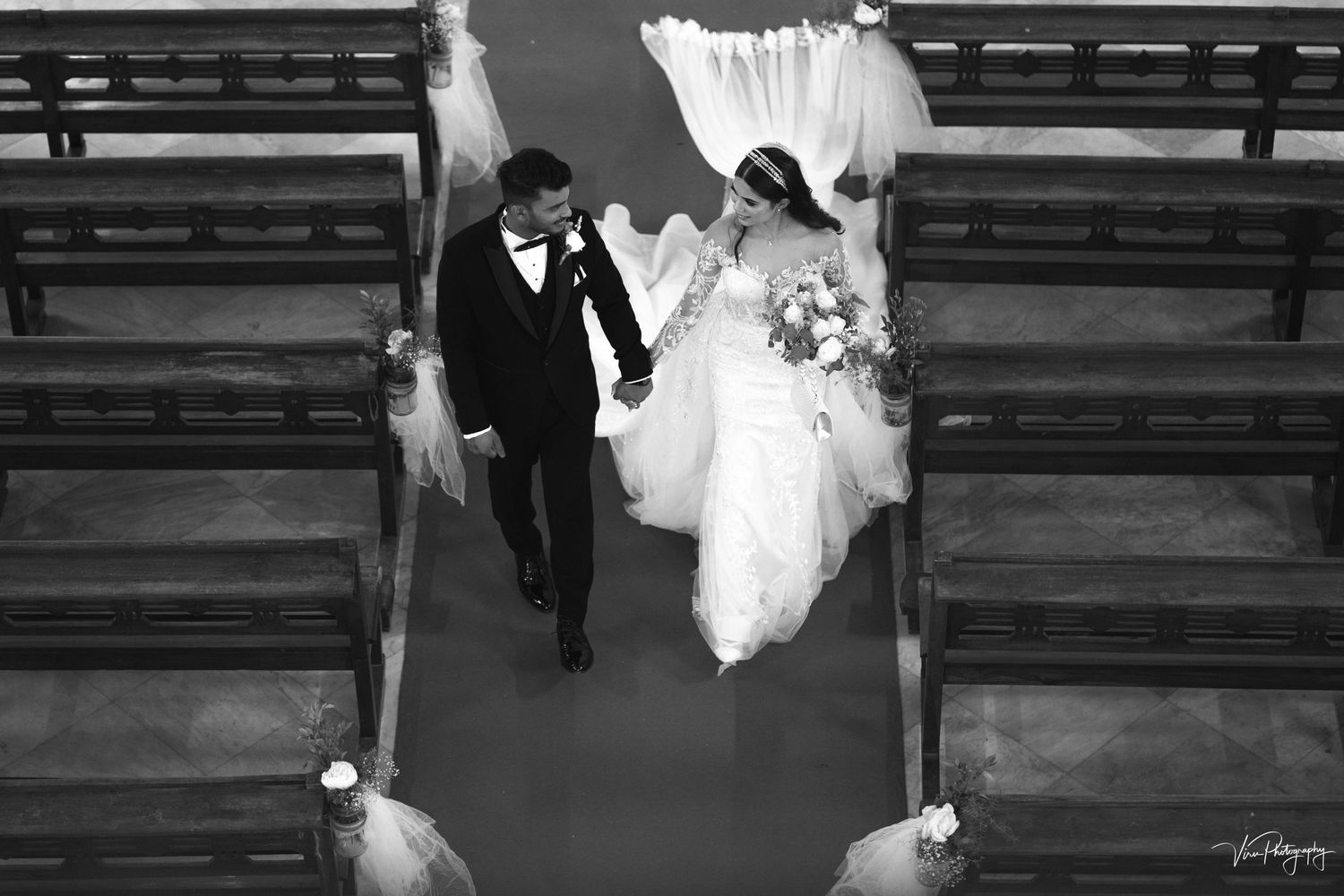 An overhead view of a wedding ceremony in a church with two people walking down the aisle between wooden pews.