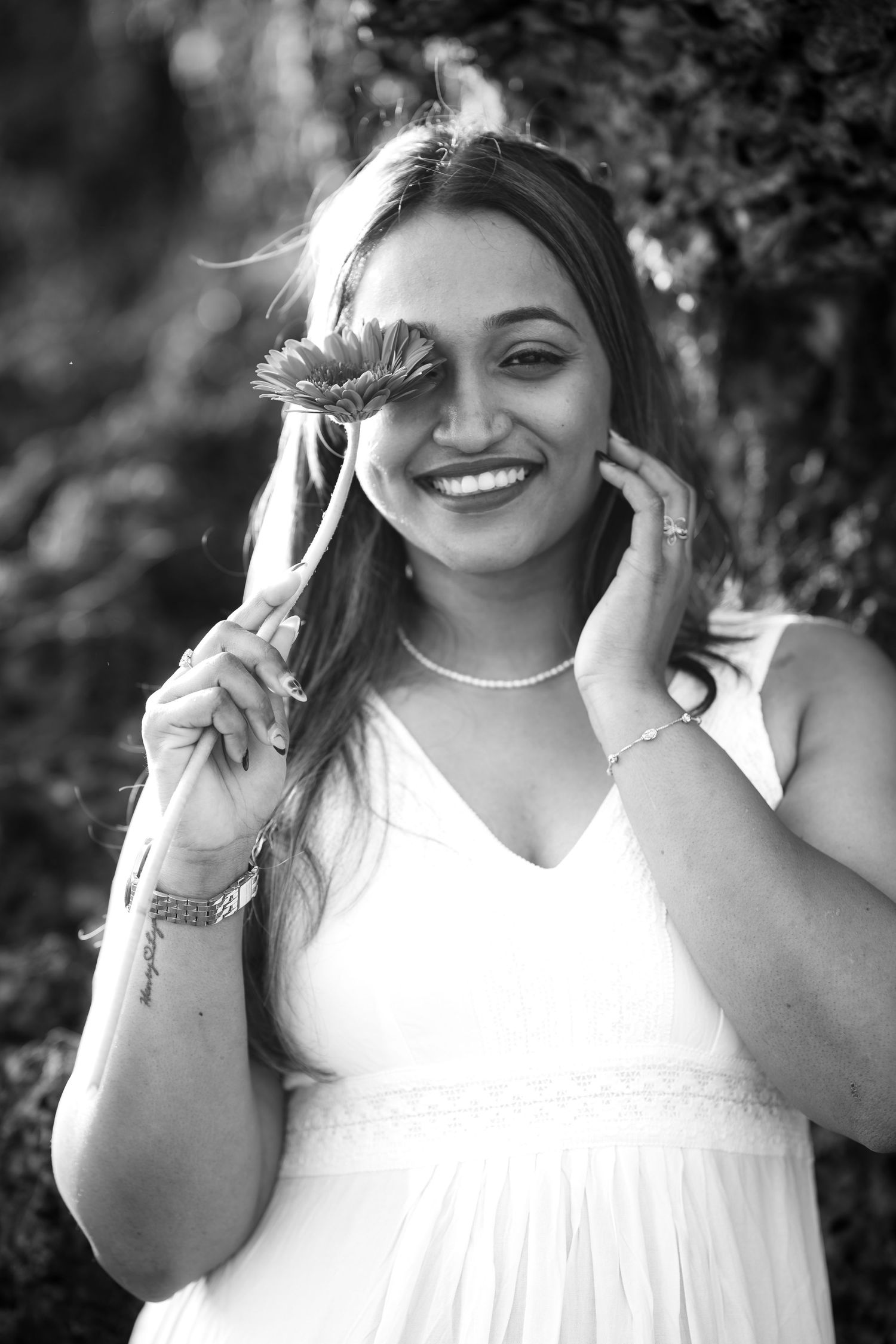 Black and white portrait of someone in a white dress holding a gerbera daisy flower, with a bright natural smile.