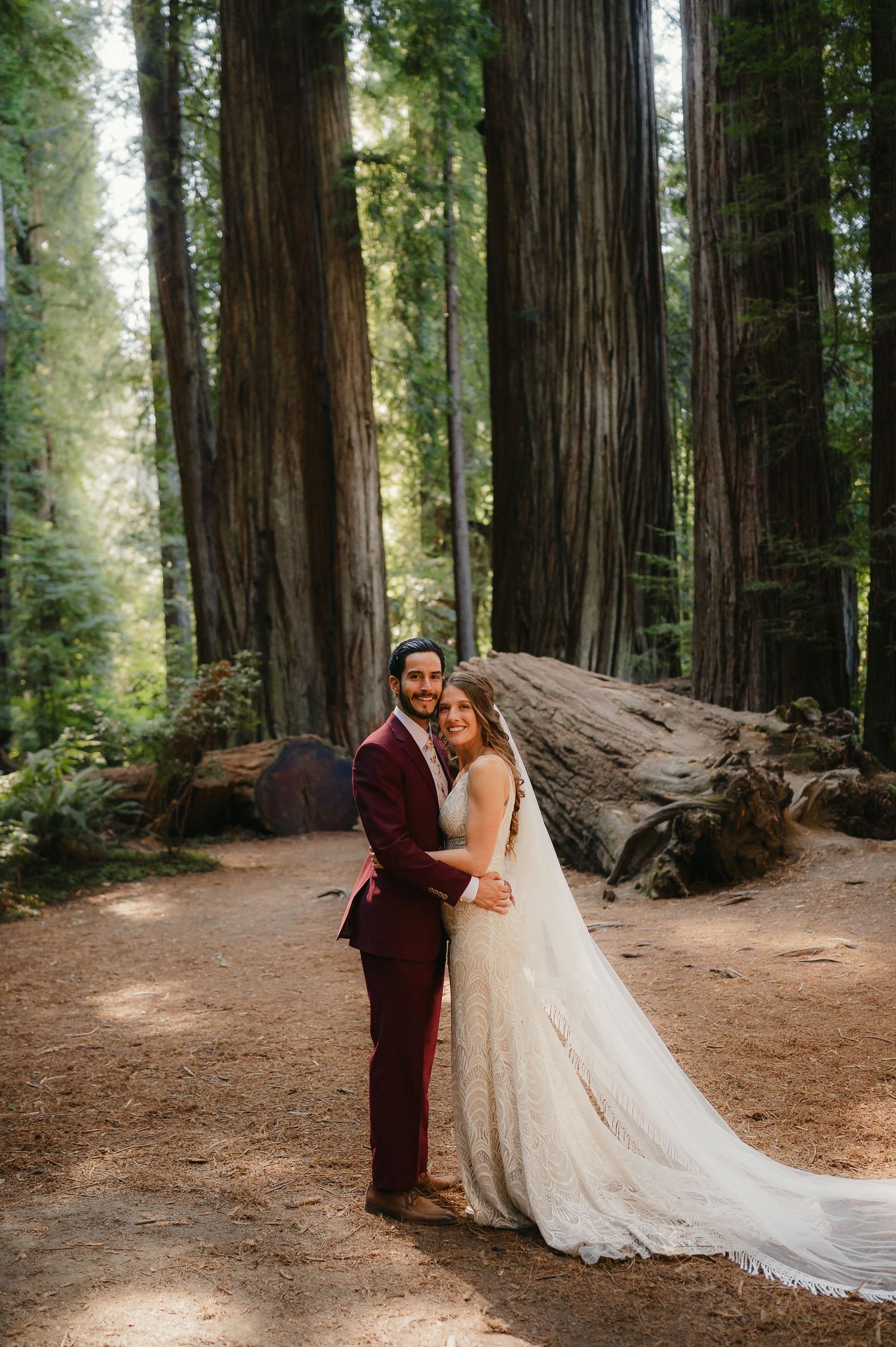 A couple shares a romantic moment among towering redwood trees in Northern California during their forest wedding celebration.