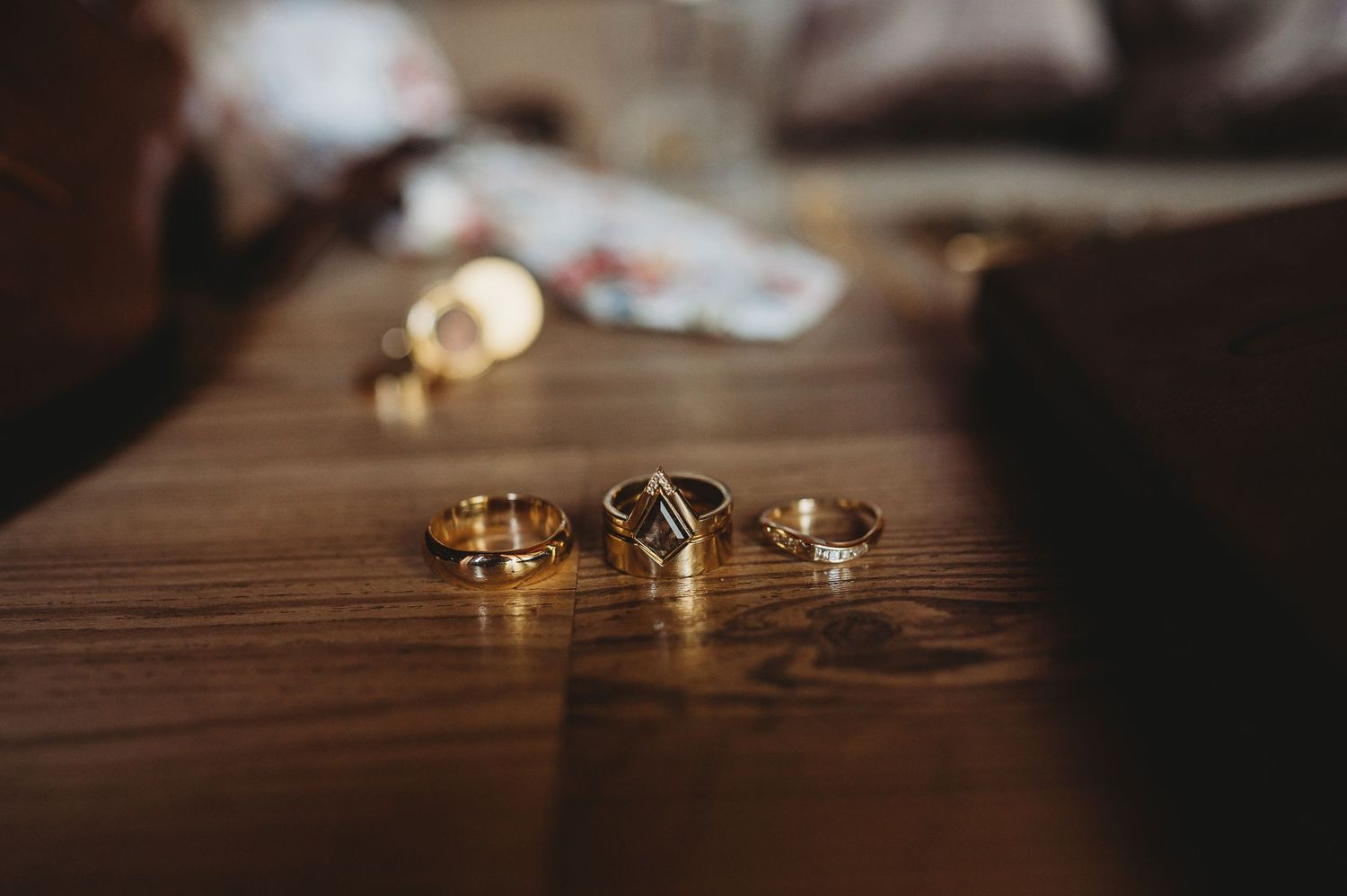 Gold wedding rings and engagement diamond ring arranged on dark wooden surface in moody lighting.