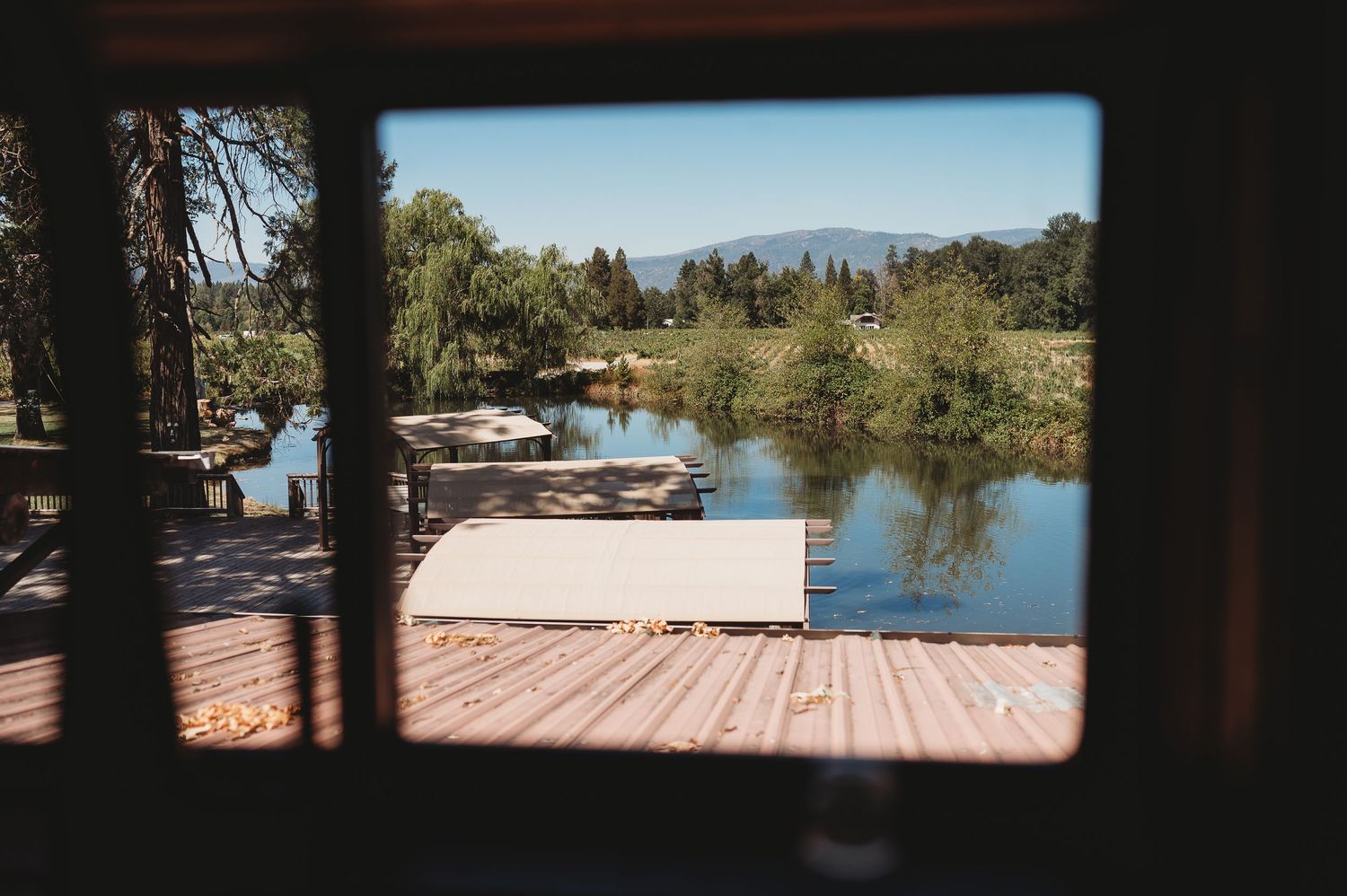 Lake view through a sunlit window opening with mountains in the distance and trees along the shore.
