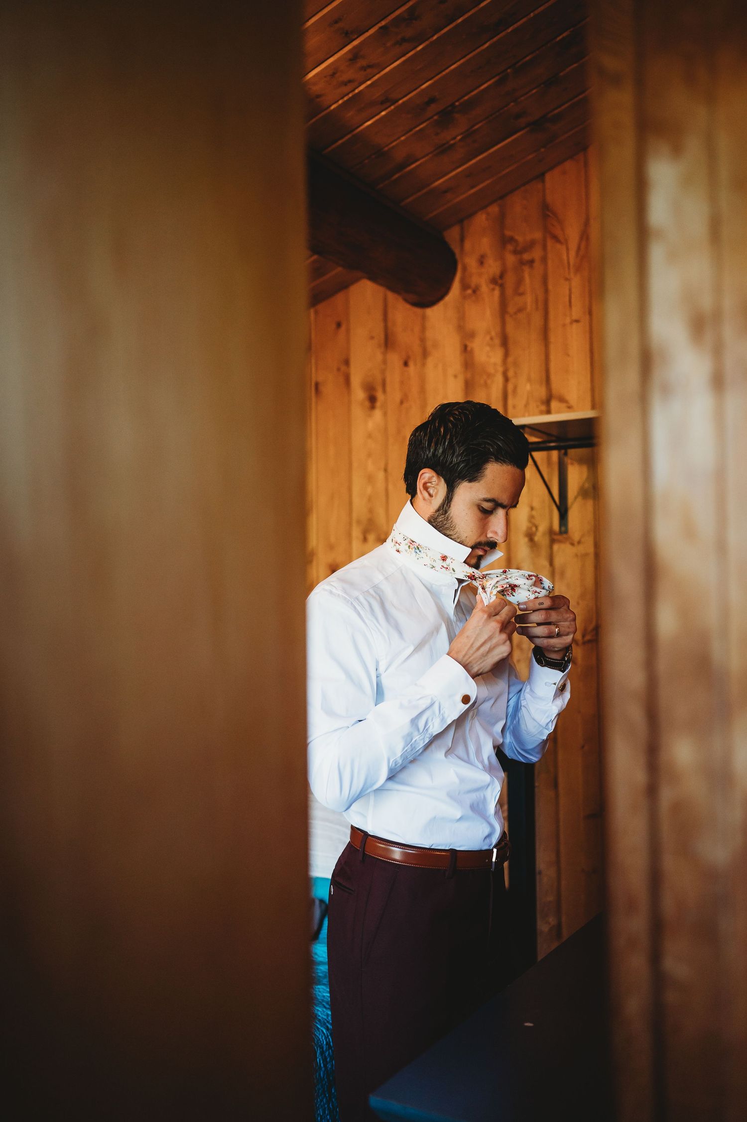 Person in white shirt and burgundy vest wiping tears while reading an emotional letter against wood paneling.