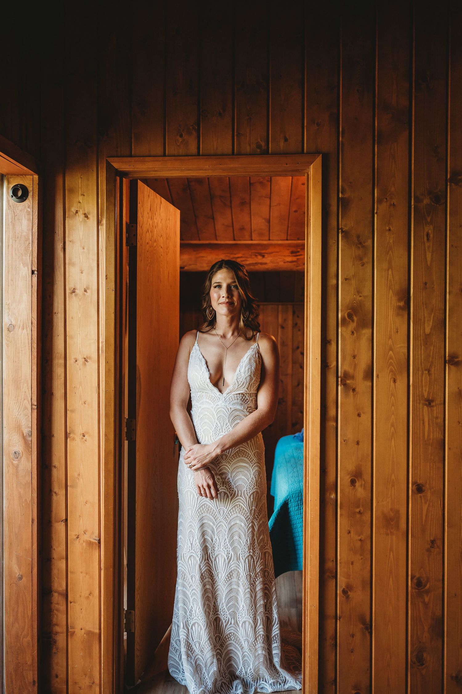 A white lace wedding dress on display against rustic wooden paneled walls with warm lighting.