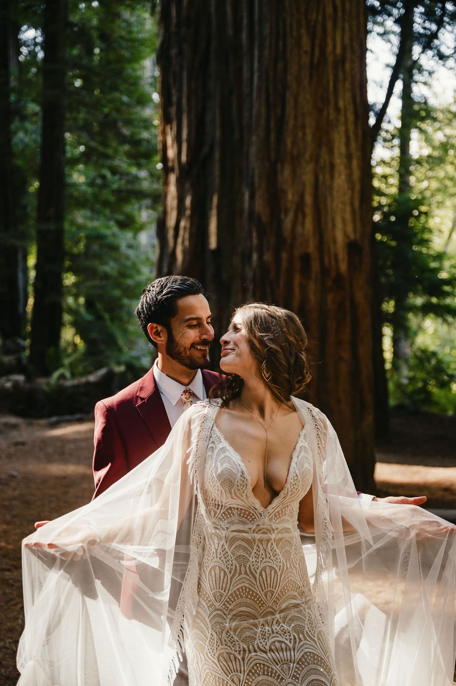 A newlywed couple embrace in a romantic dance under towering redwood trees in a dreamy forest setting.