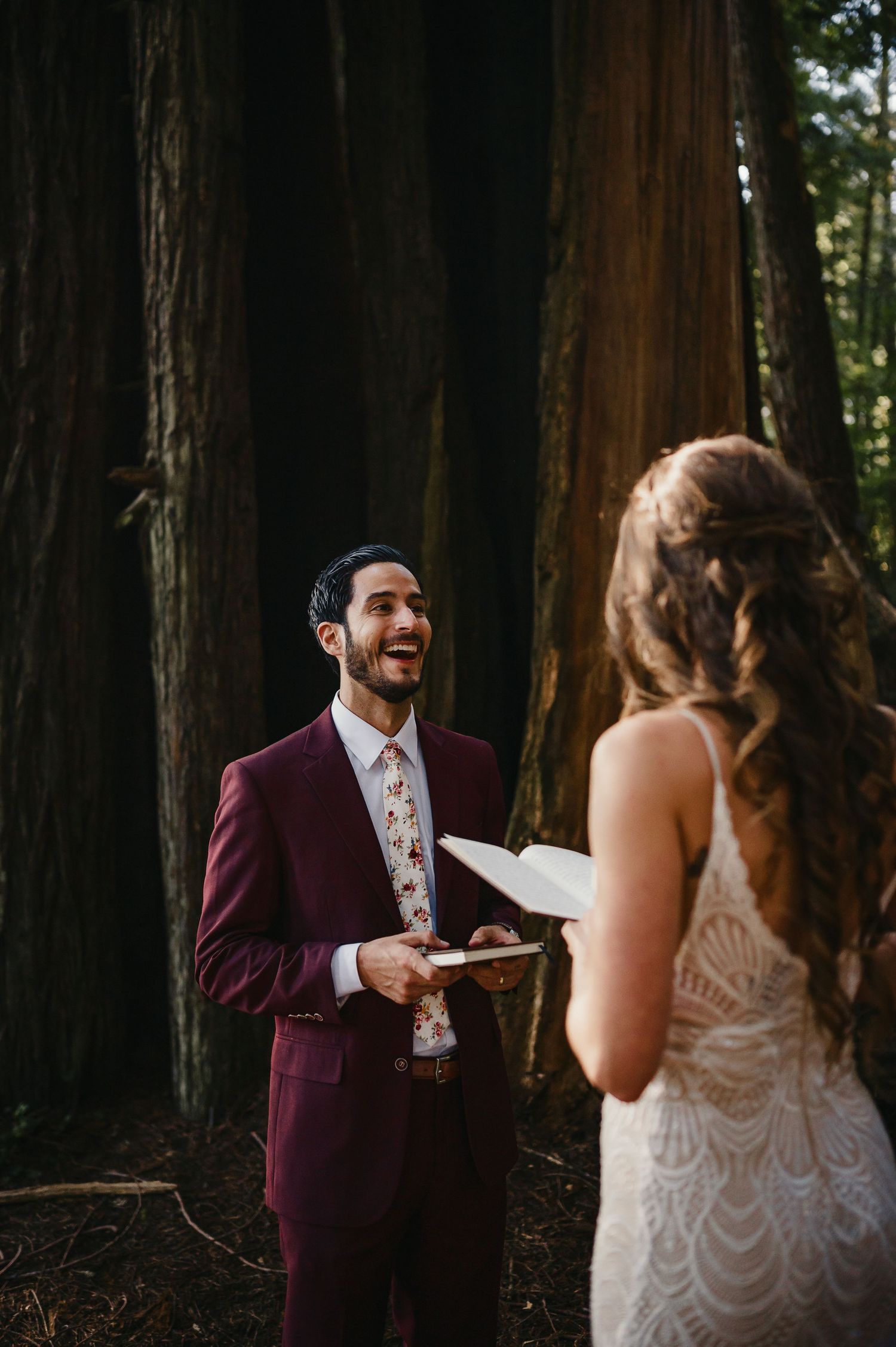 A couple shares an emotional first look moment among towering redwood trees in a forest.