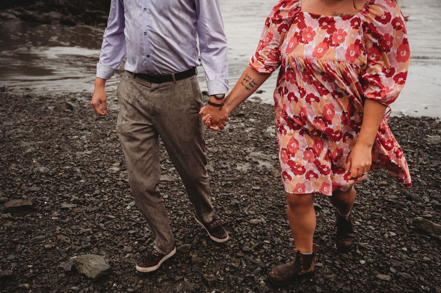 A couple holding hands walking together on rocky terrain, with one wearing a floral dress and another in casual attire.