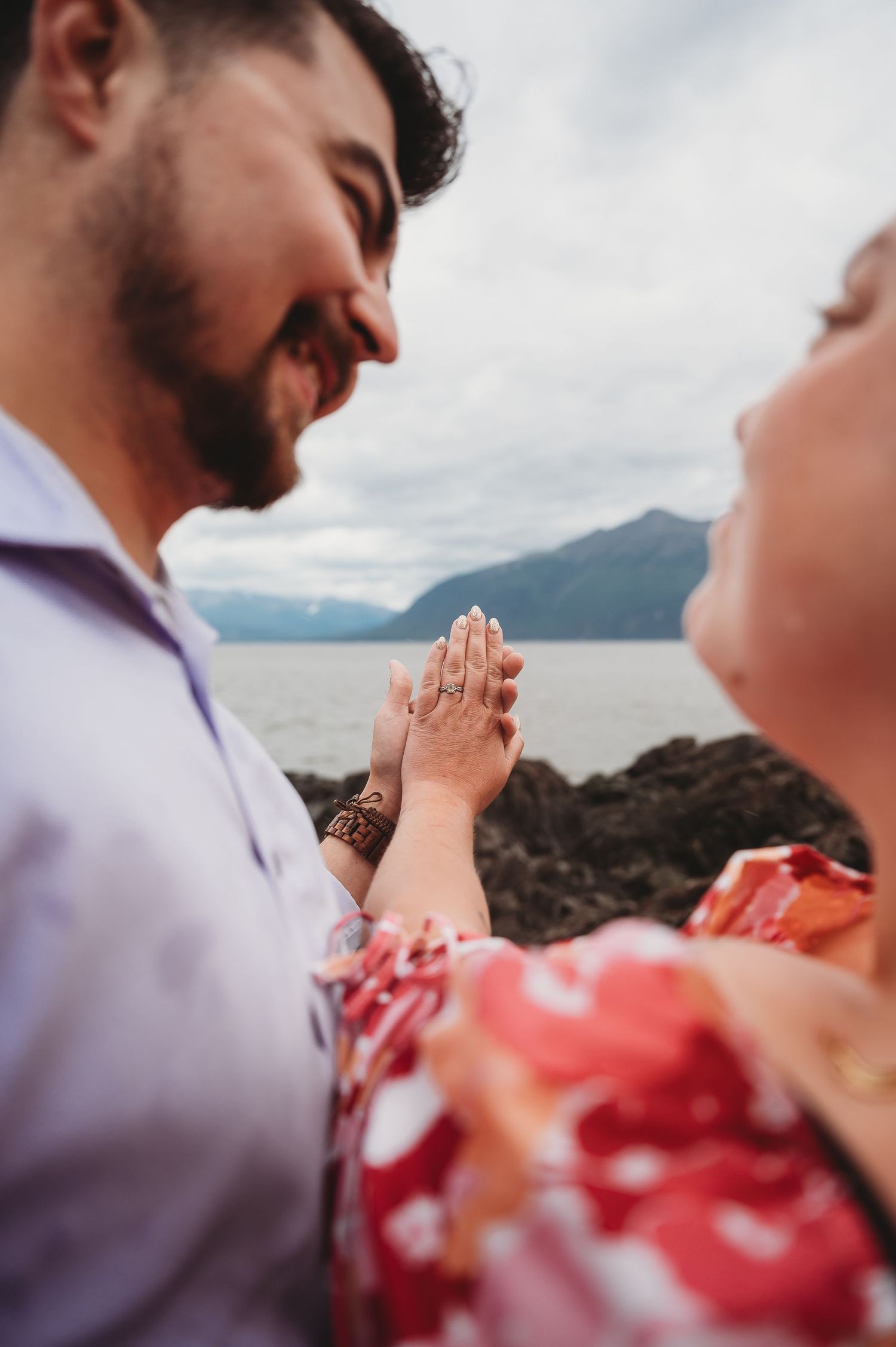 Two people share an intimate moment against a scenic mountain and water backdrop at sunset.