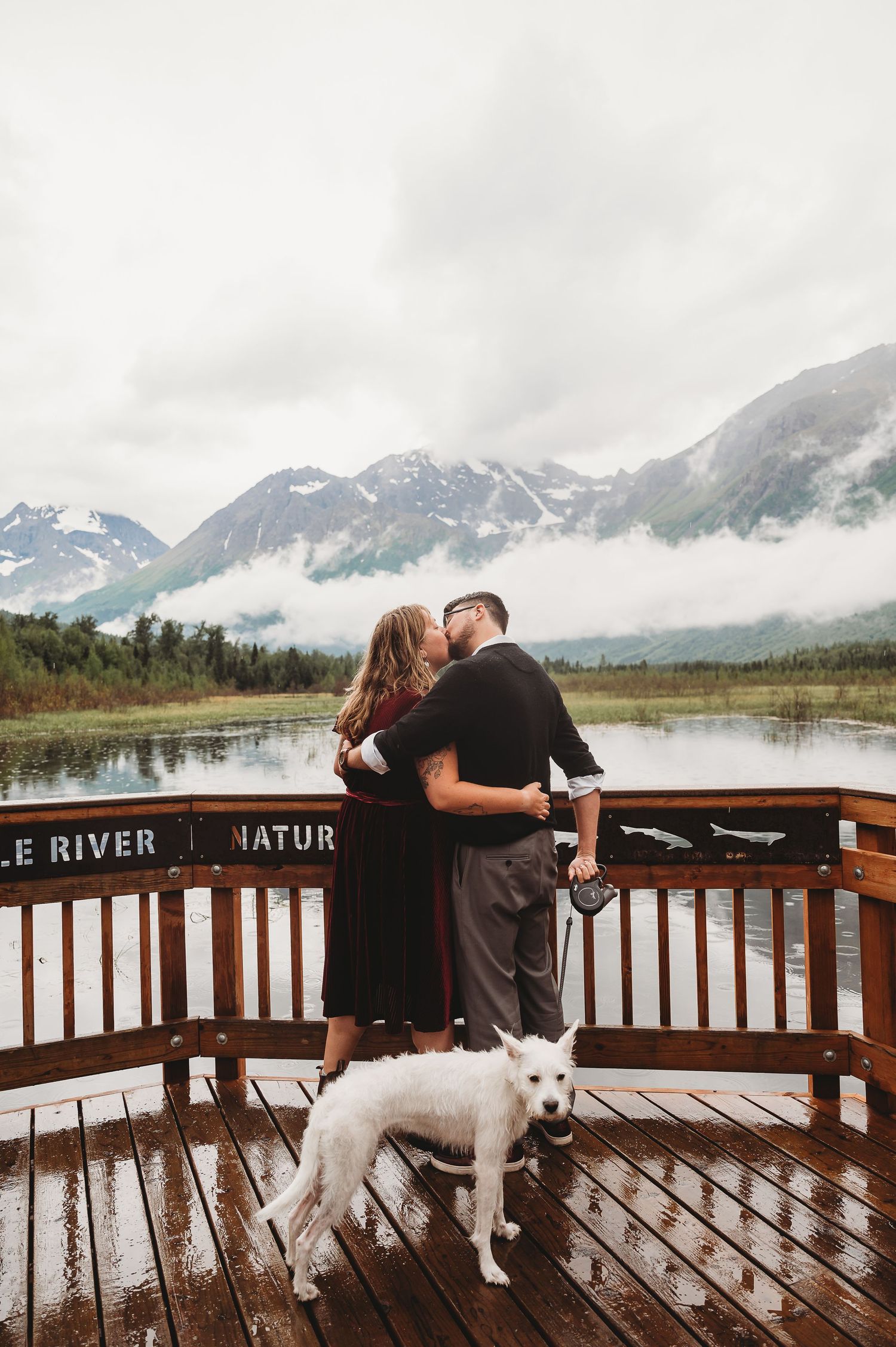 People share a moment on Eagle River observation deck with mountains and glacier views in background.
