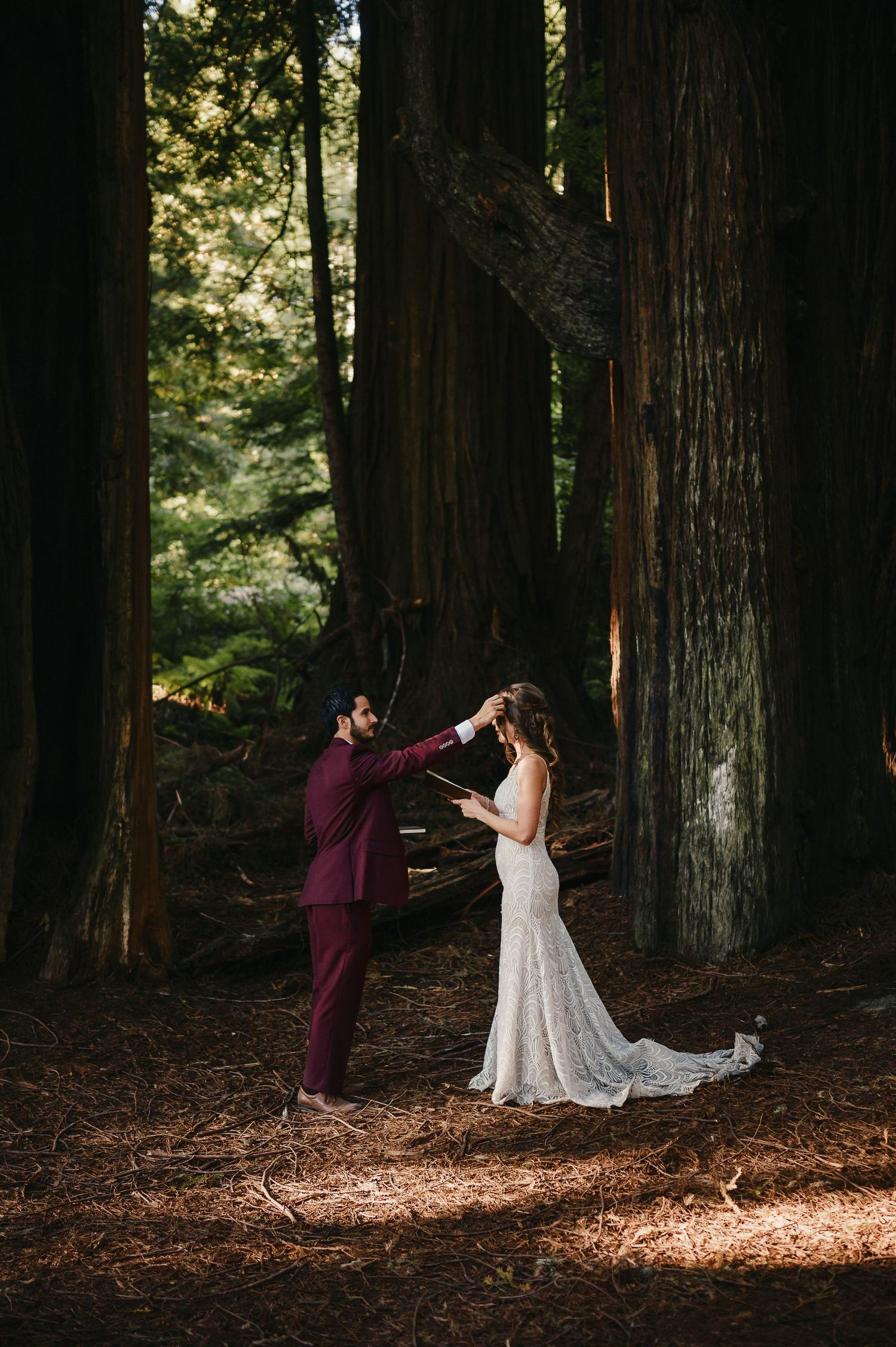 A romantic wedding couple dances together in a serene redwood forest with sunlight streaming through the trees.