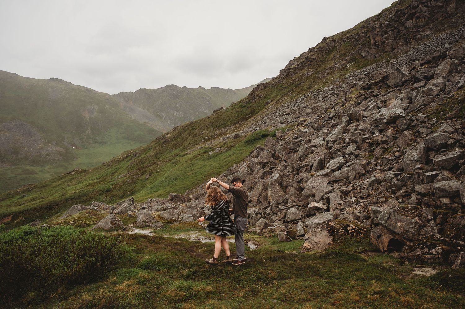 A hiking path winds through rocky mountain terrain under cloudy skies.