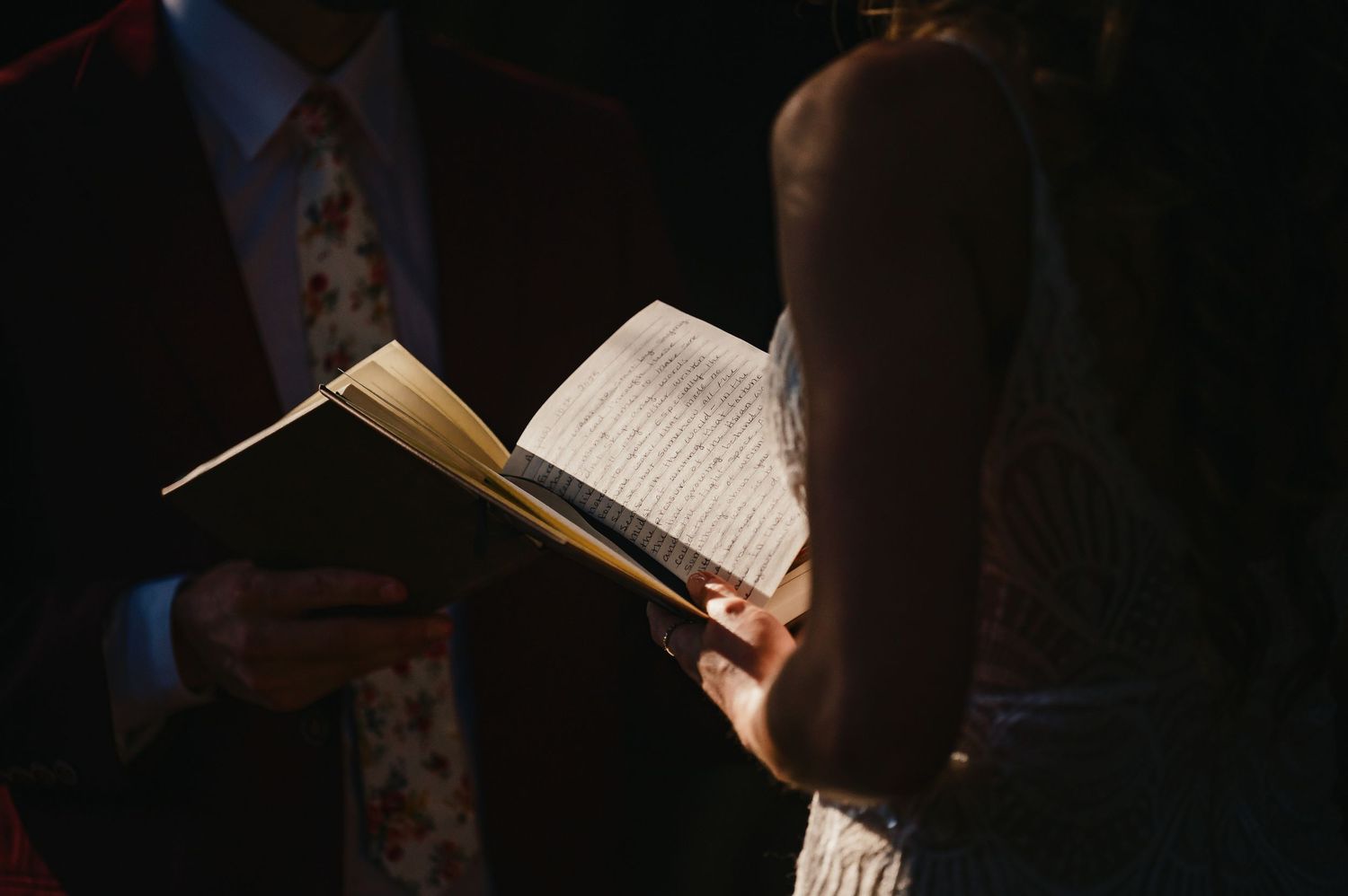 Two people read from books together in a dimly lit setting.