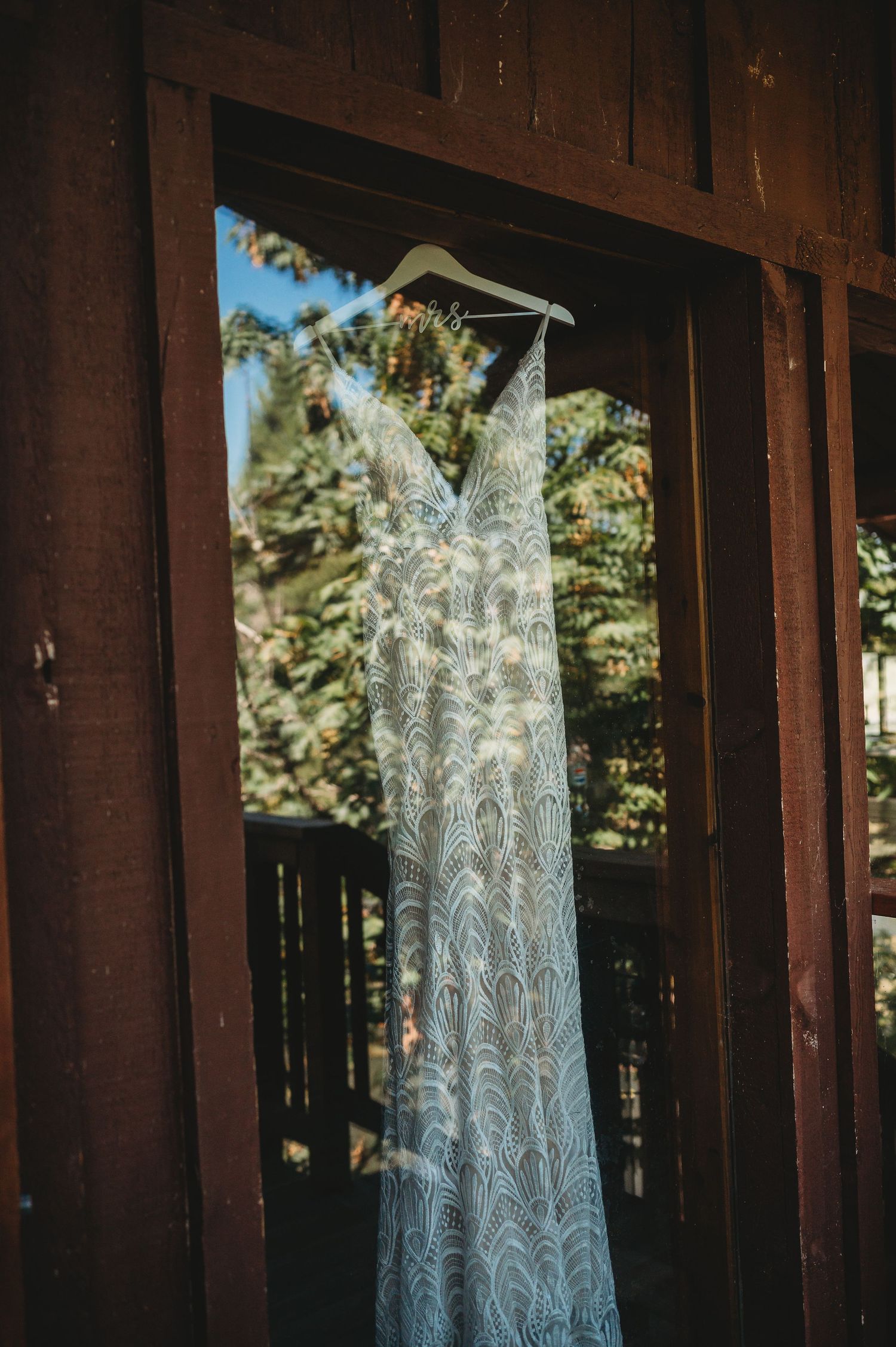 Elegant lace wedding gown displayed against rustic cabin windows with natural light streaming through.