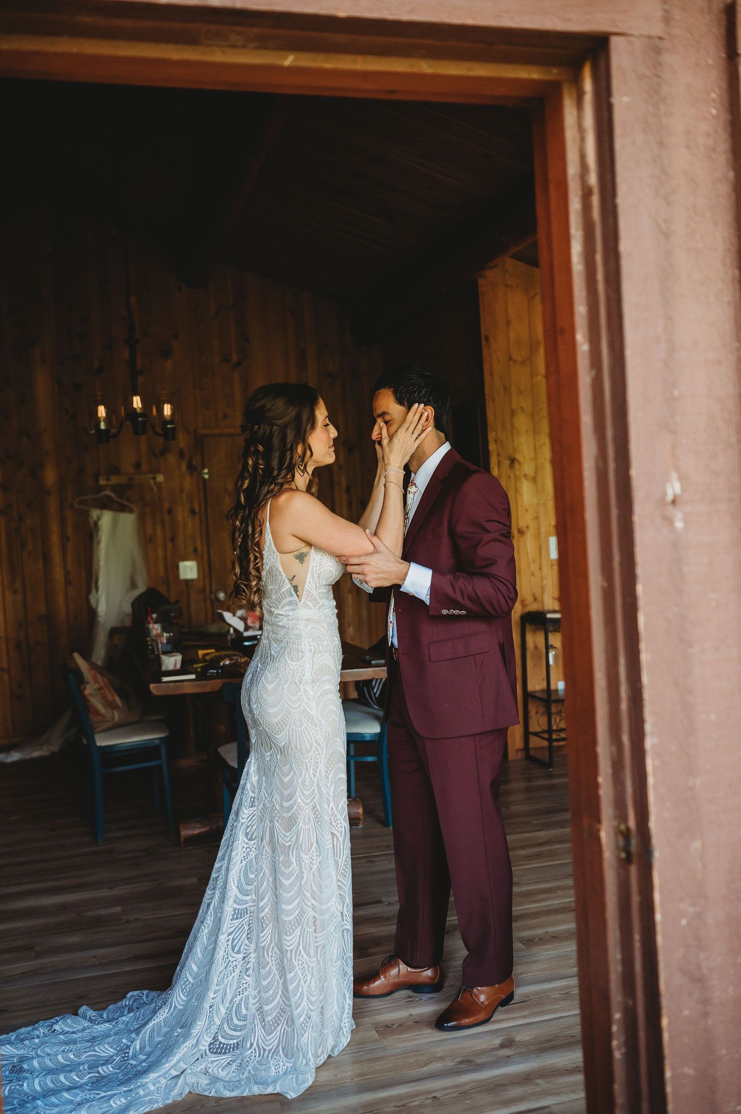 A wedding couple sharing their first look in a rustic wooden venue with burgundy and light blue attire.