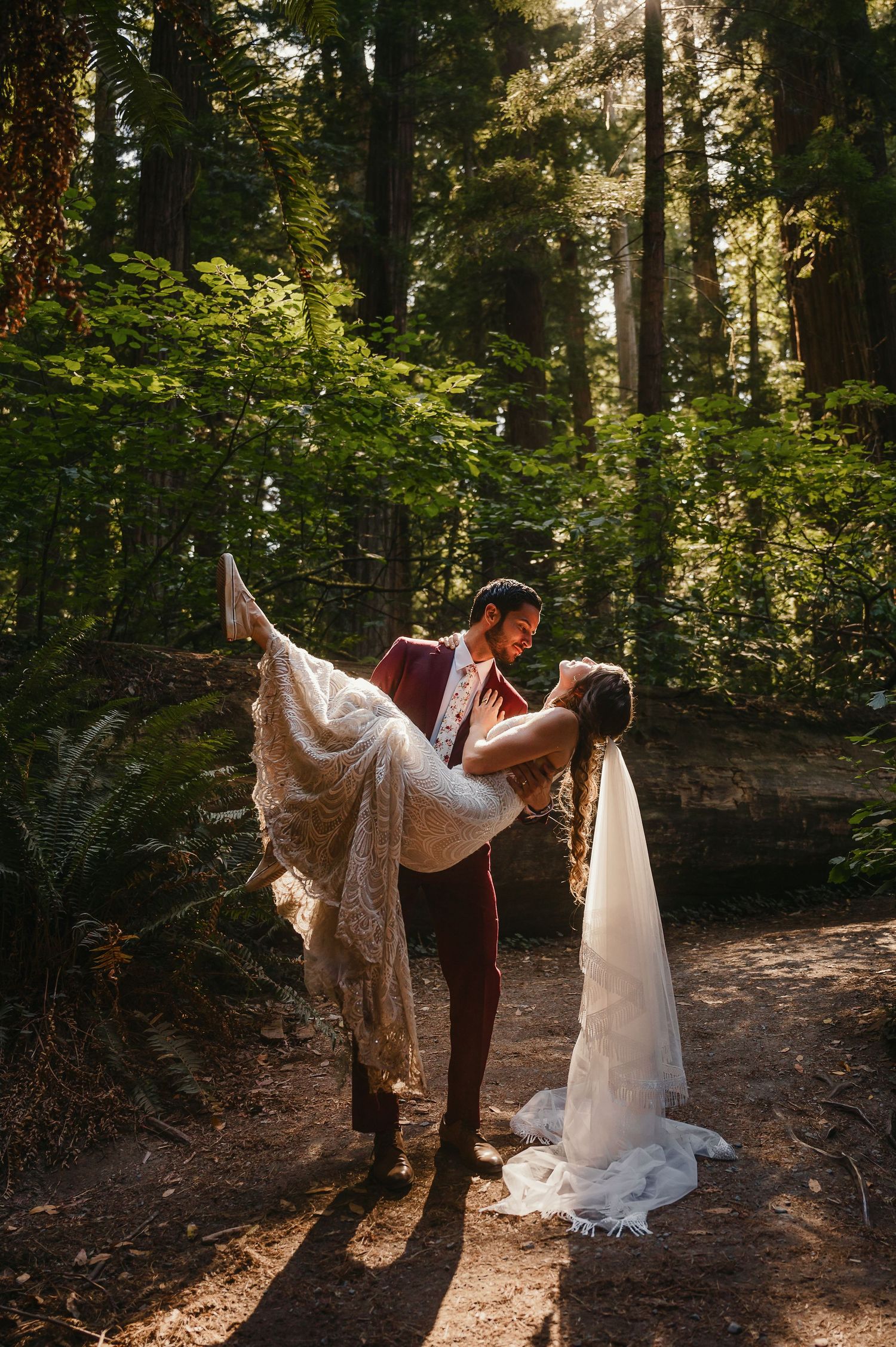 Romantic couple dances together in a sunlit forest clearing surrounded by tall evergreen trees.