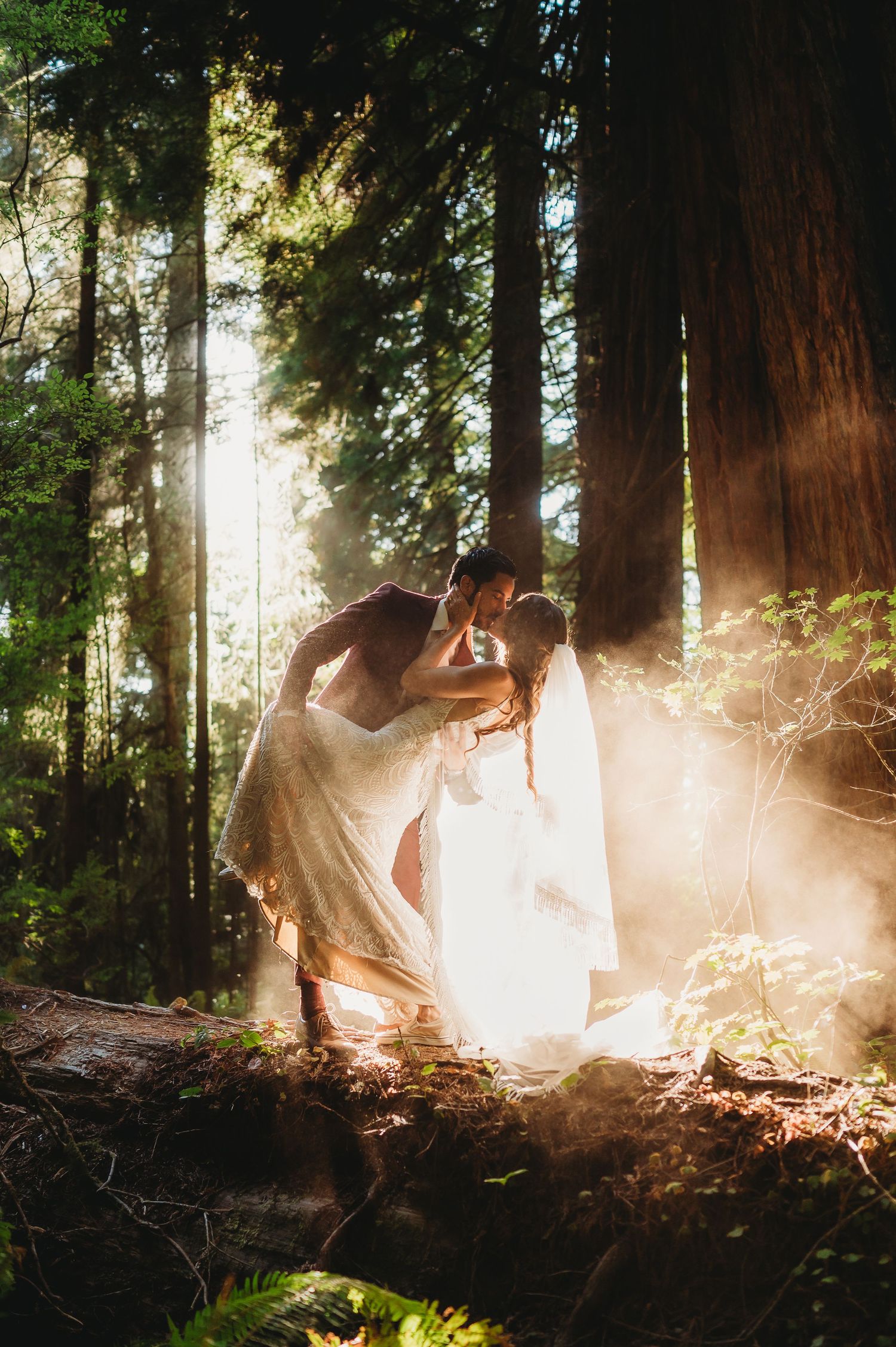 Two dancers in white flowing dresses perform an ethereal dance in a sunlit redwood forest.