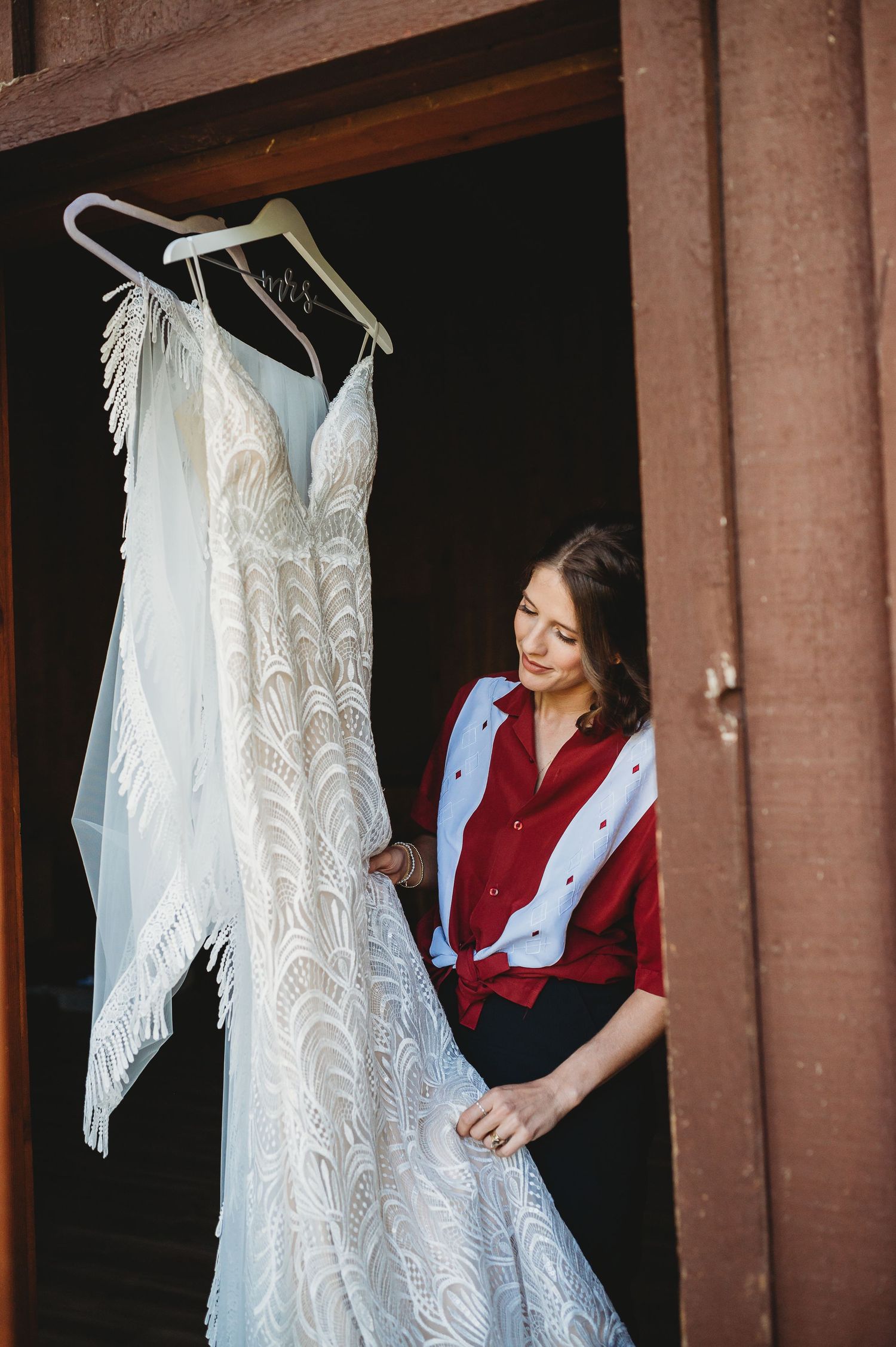 Wedding dress with delicate lace details hangs on display against a rustic brown exterior wall.
