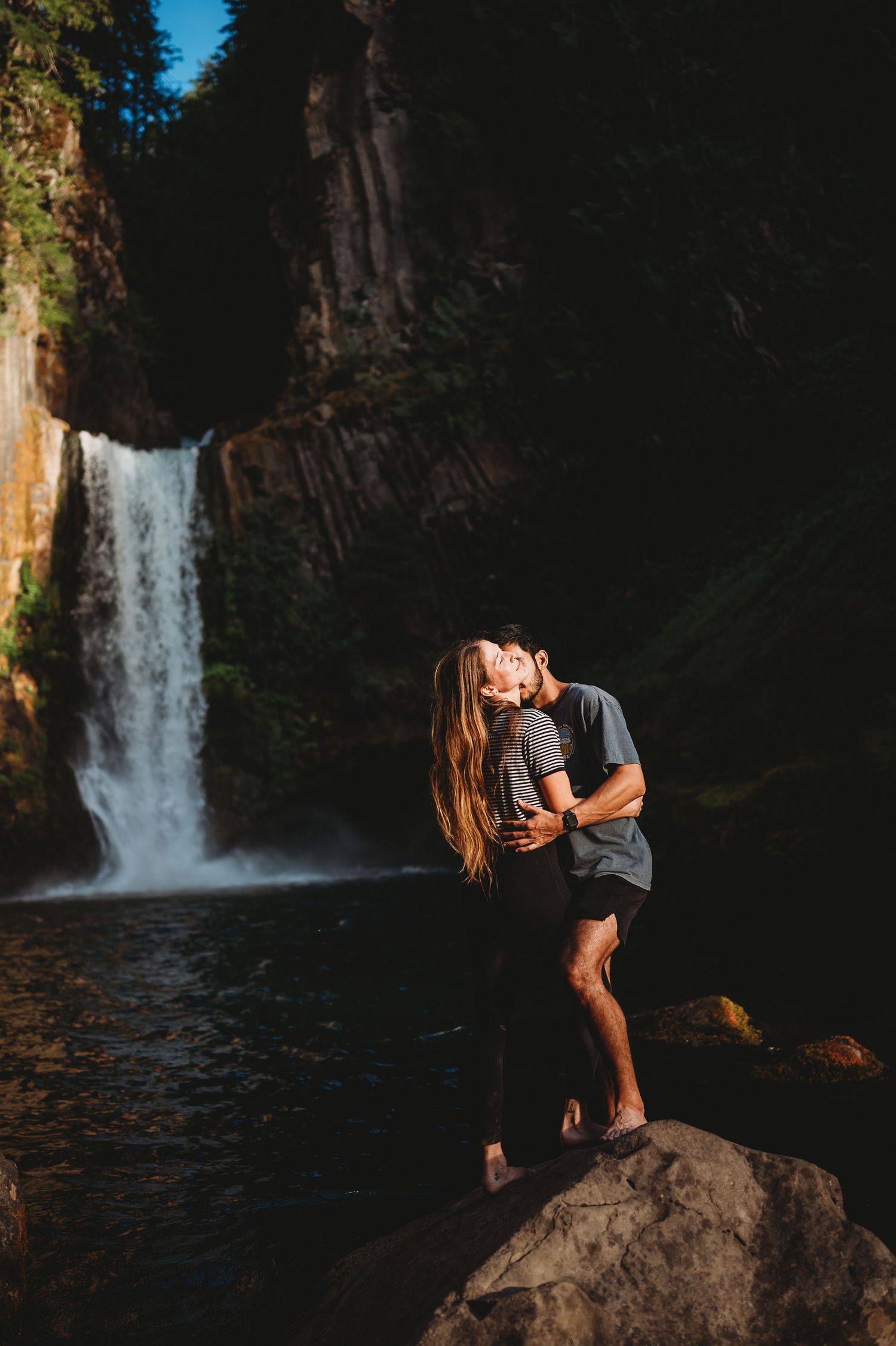 A couple shares romantic moments by a scenic waterfall in a series of silhouetted photos at sunset.